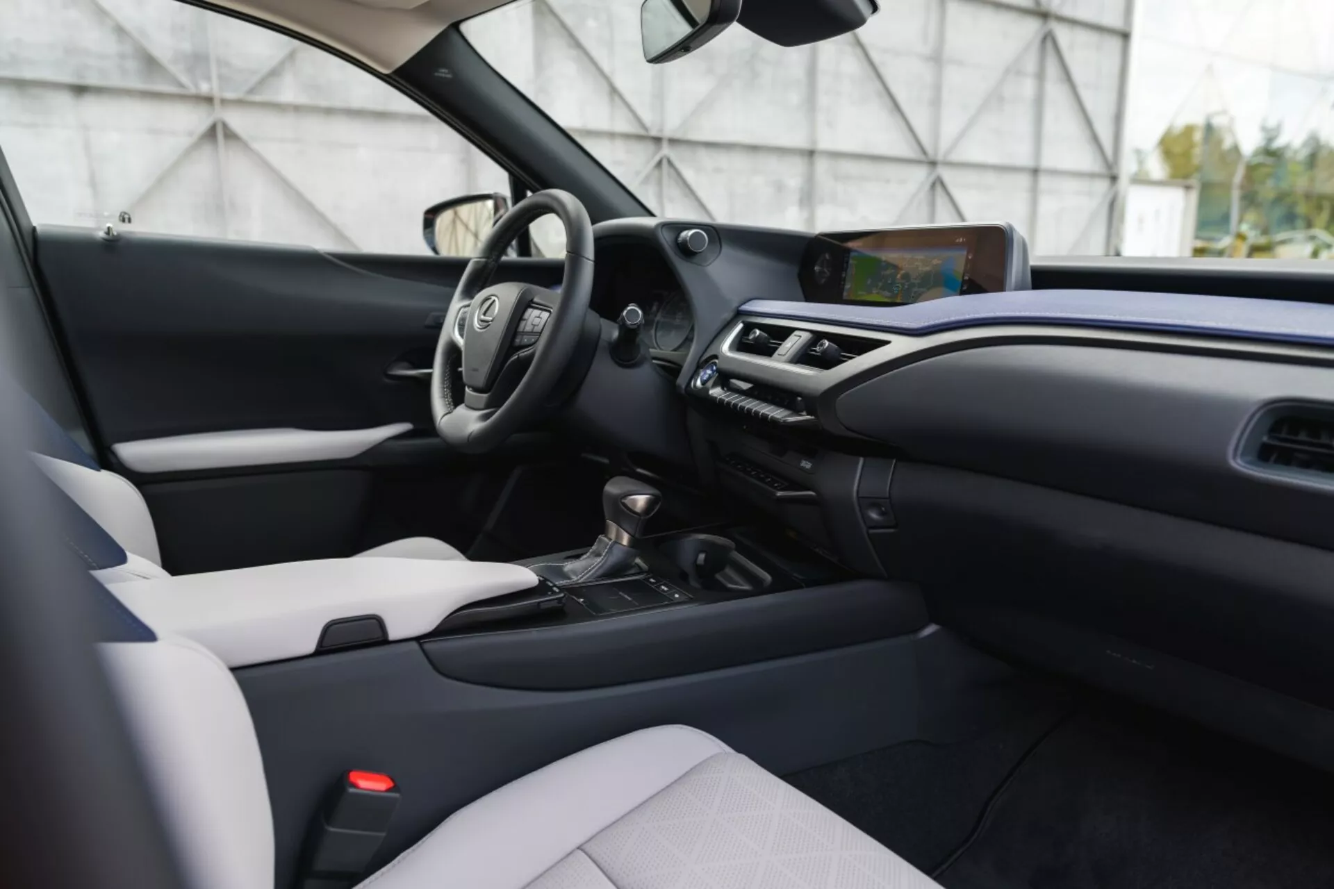 Notranjost modernega Lexusa UX 2019 s dvobarvnim dizajnom, multifunkcijskim volanom, izstopajočim zaslonom za infotainment in avtomatskim menjalnikom iz nekoliko ekscentrične perspektive, na višini oči
