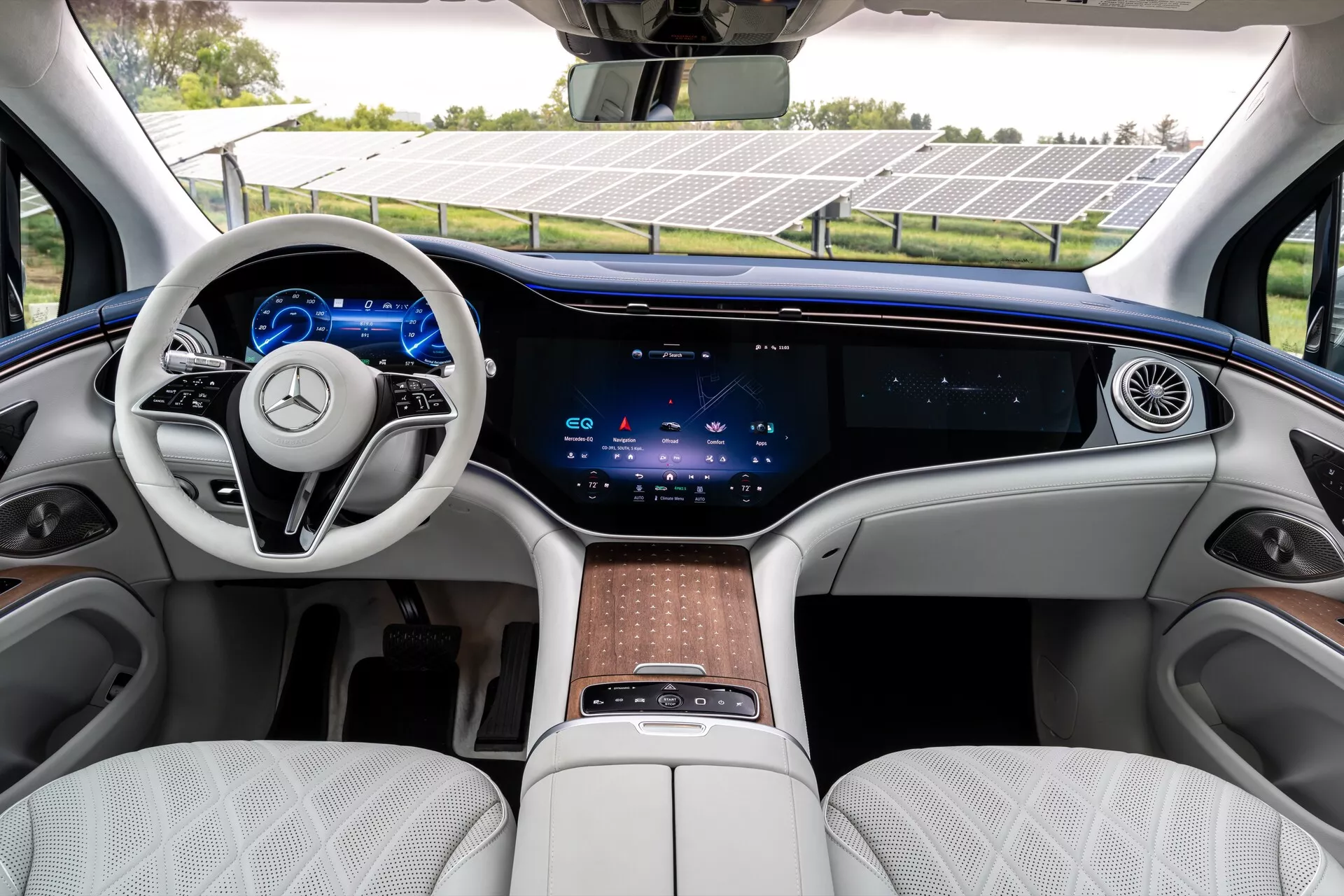 Notranjost Mercedes EQS-SUV 2022, ki prikazuje razkošno sprednjo vrstico z dvokrakim volanom, integriranimi na dotik občutljivimi kontrolami, popolnoma digitalnimi merilniki, obsežnim osrednjim zaslonom na dotik, ki sega čez celotno armaturo, minimalnimi fizičnimi kontrolami za klimatski sistem, neprekinjenim zračnikom, belimi prešitimi usnjenimi sedeži, lesenimi oblogami in osrednjo konzolo z na dotik občutljivo ploščo in shranjevalnim prostorom.