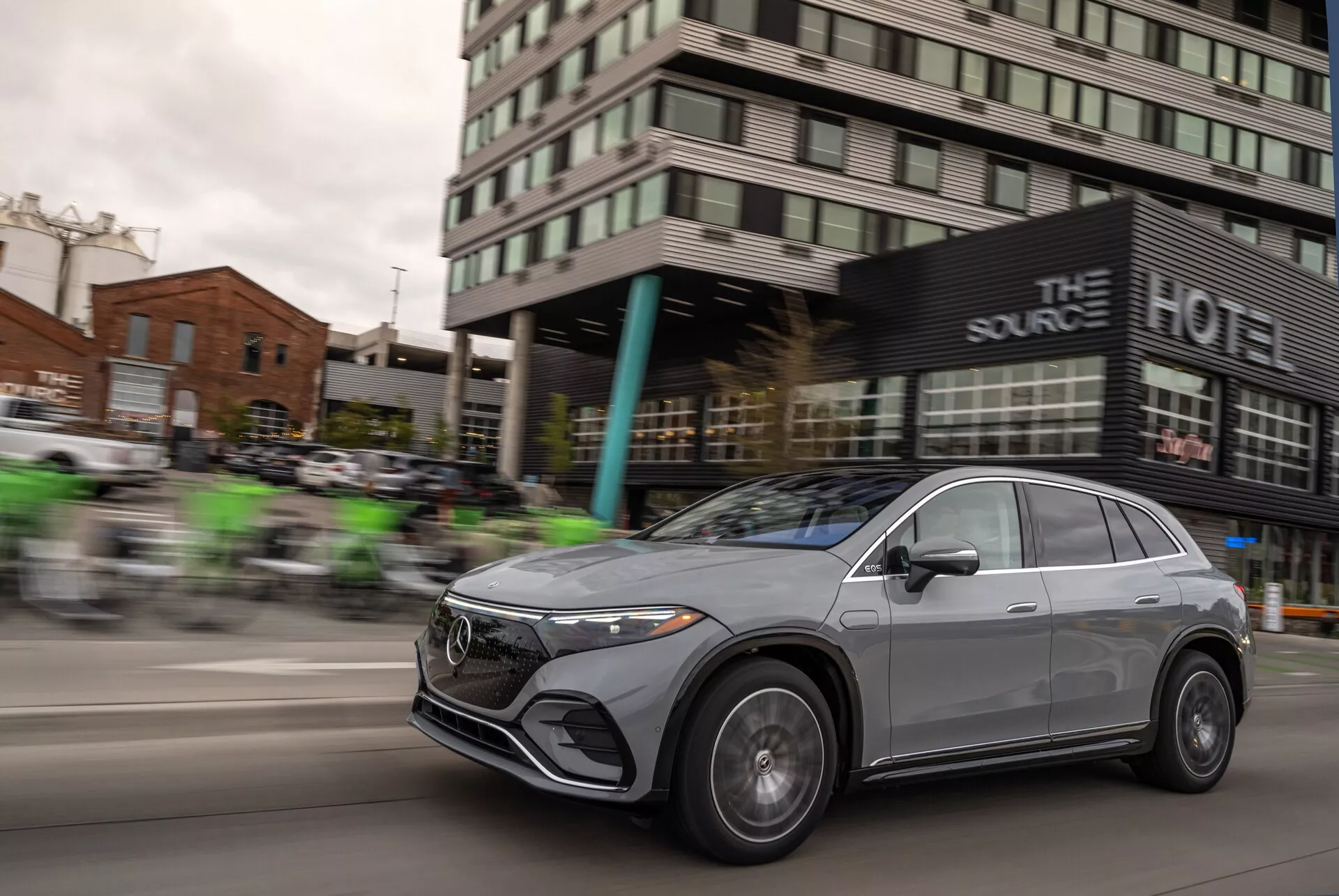 Dinamičen posnetek Mercedes EQS-SUV 2022 v gibanju s panoramskim zameglitvenim učinkom, ki poudarja hitrost vozila. Med vidne elemente sodijo sprednja rešetka, LED žarometi, aluminijasta kolesa in aerodinamična zasnova pokrova motorja ter strešne linije, kar poudarja prefinjene in luksuzne elemente vozila. Kovinska premaz avtomobila in slog crossover z elegantnimi, brezokvirnimi okni ter aerodinamično oblikovanimi ogledali doda njegovemu sodobnemu in prestižnemu videzu.