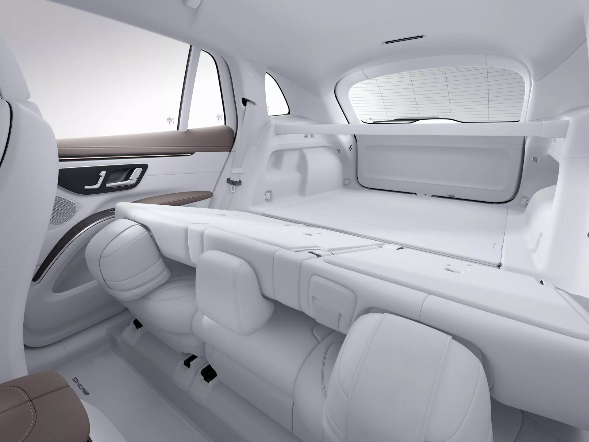 Notranji pogled Mercedes EQS SUV 2022, osredotočen na zadnje sedeže in del prtljažnika. Slika je posneta iz poševnega kota, nekoliko nad višino sedežev, kaže razporeditev sedežev in prostor. Monokromatični beli ton poudarja čist, moderen dizajn. Zadnji sedeži so v klopi konfiguraciji s tremi nastavljivimi nasloni za glavo in posameznimi varnostnimi pasovi. Stranska vrata imajo leseno oblogo in integrirane kontrole, potencialno za okna ali druge elektronske funkcije. Zadnje okno ima senčilo, vidna pa je tudi ravna polica, kar poudarja udobje potnikov in luksuzne značilnosti.