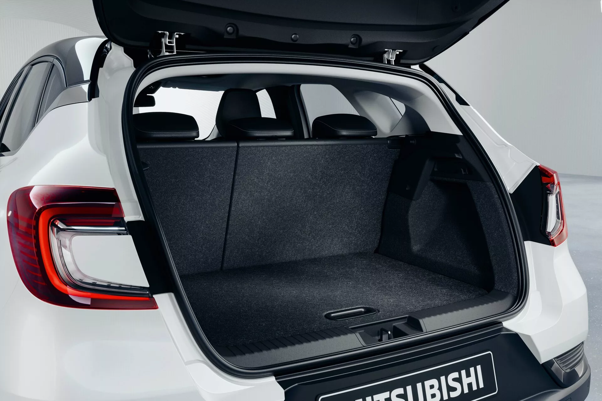 Zadnji predel Mitsubishi ASX 2023 (2. generacija) prikazuje odprt prtljažnik iz rahlo zvišanega kota, poudarjajoč preprosto tovorno površino, mehanizem tečaja, ravno nakladalno tla in delno vidne moderne LED zadnje luči z logotipom Mitsubishi na prtljažnih vratih.