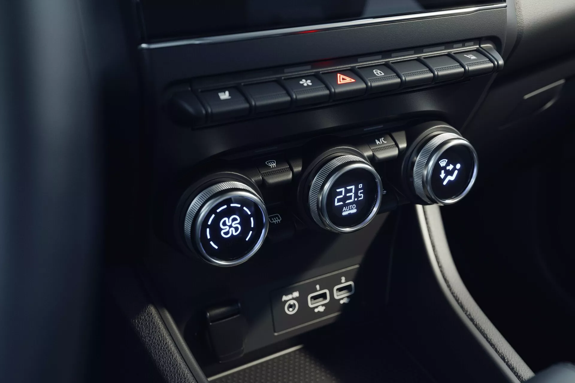 Pogled od blizu na notranji sistem za nadzor klime pri Mitsubishi ASX 2023 (2. generacija). Slika, posneta z rahlo dvignjenega kota, se osredotoča na osrednjo konzolo s tremi gumbi za nadzor temperature - levi nastavljen na 'LO' in desni na '23.5'. Sredinski gumb verjetno nadzoruje hitrost ali smer ventilatorja. Nad gumbi so stikala za odmrzovanje stekel, opozorilne lučke in kroženje zraka. Spodaj so sodobni USB vhodi. Oblikovanje je minimalistično s črnimi elegantnimi površinami.