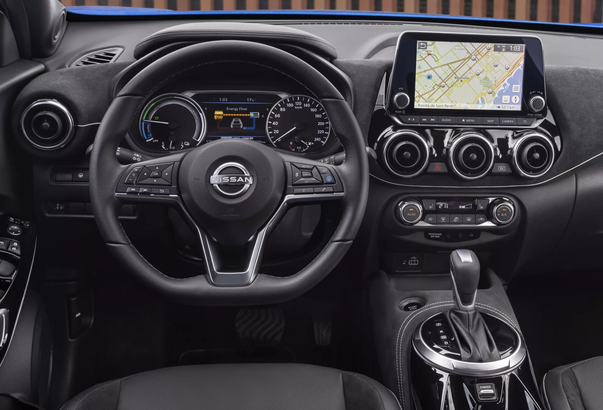 Pogled na notranjost Nissan Juke (F16) letnik 2019, ki poudarja armaturno ploščo, multifunkcijski volan s tremi kraki z logotipom NISSAN, digitalno-analogni instrumentni sklop, zaslon na dotik z navigacijskim sistemom, dvopodročno klimatsko napravo in območje avtomatskega prestavnika.