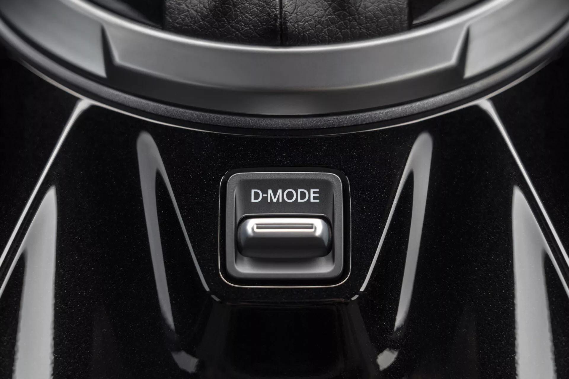 Pogled od blizu na gumb D-MODE na sredinski konzoli Nissan Juke 2019 (F16), s sijajnim črnim zaključkom in kromiranimi poudarki pod zgornjo osvetlitvijo