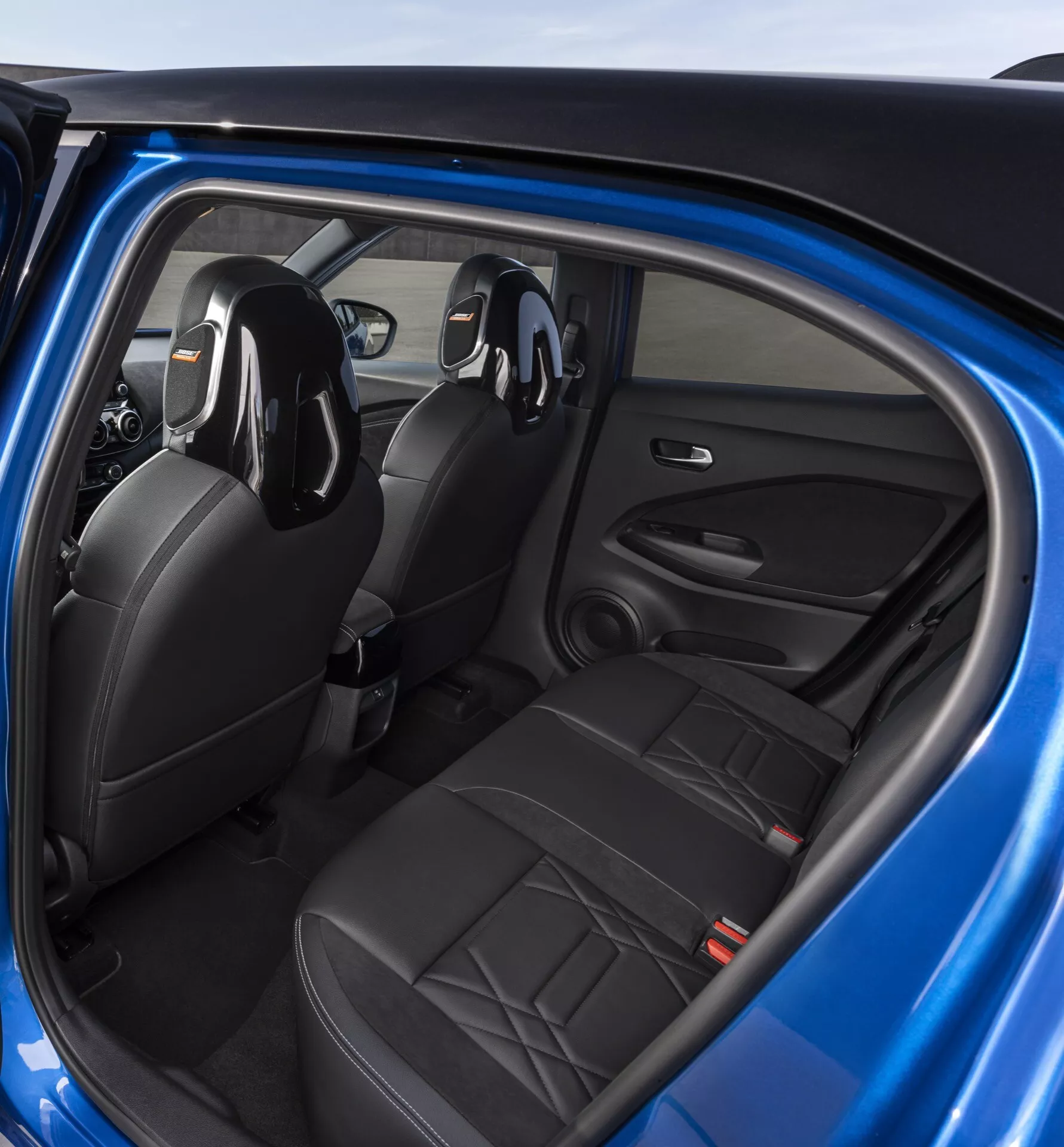 Notranjost Nissan Juke 2019 (F16) iz perspektive zadnjega potnika, ki prikazuje črna usnjena sedeža, kontrole na vratih voznika in integriran avdio sistem
