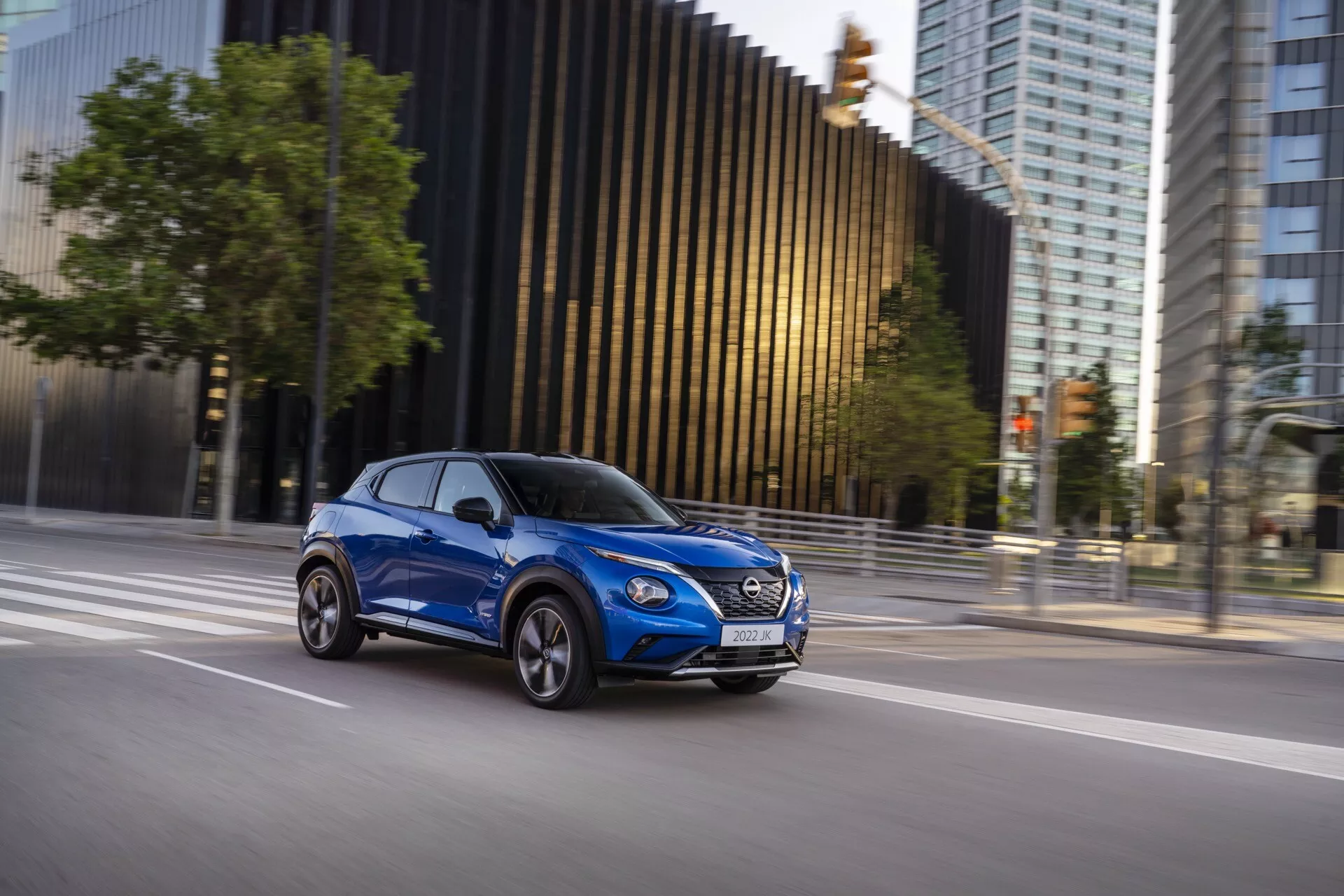Moderen kompaktni SUV Nissan Juke (F16) iz leta 2019 v gibanju, posnet z bočne perspektive v svetlo modri barvi, ki poudarja obliko vozila, dinamično prisotnost in aerodinamične značilnosti na mestnem ozadju.