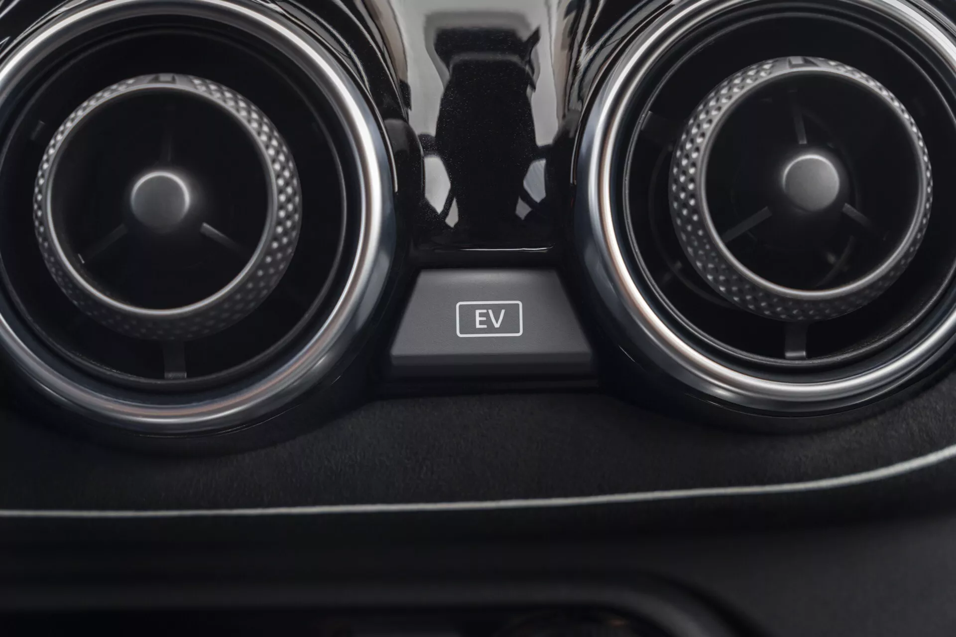 Pogled od blizu na notranjost Nissan Juke 2019 (F16), osredotočen na prezračevalne reže klimatske naprave in gumb za EV način med njimi, ki prikazuje klimatsko kontrolo avtomobila in tehnologijo električnih vozil.