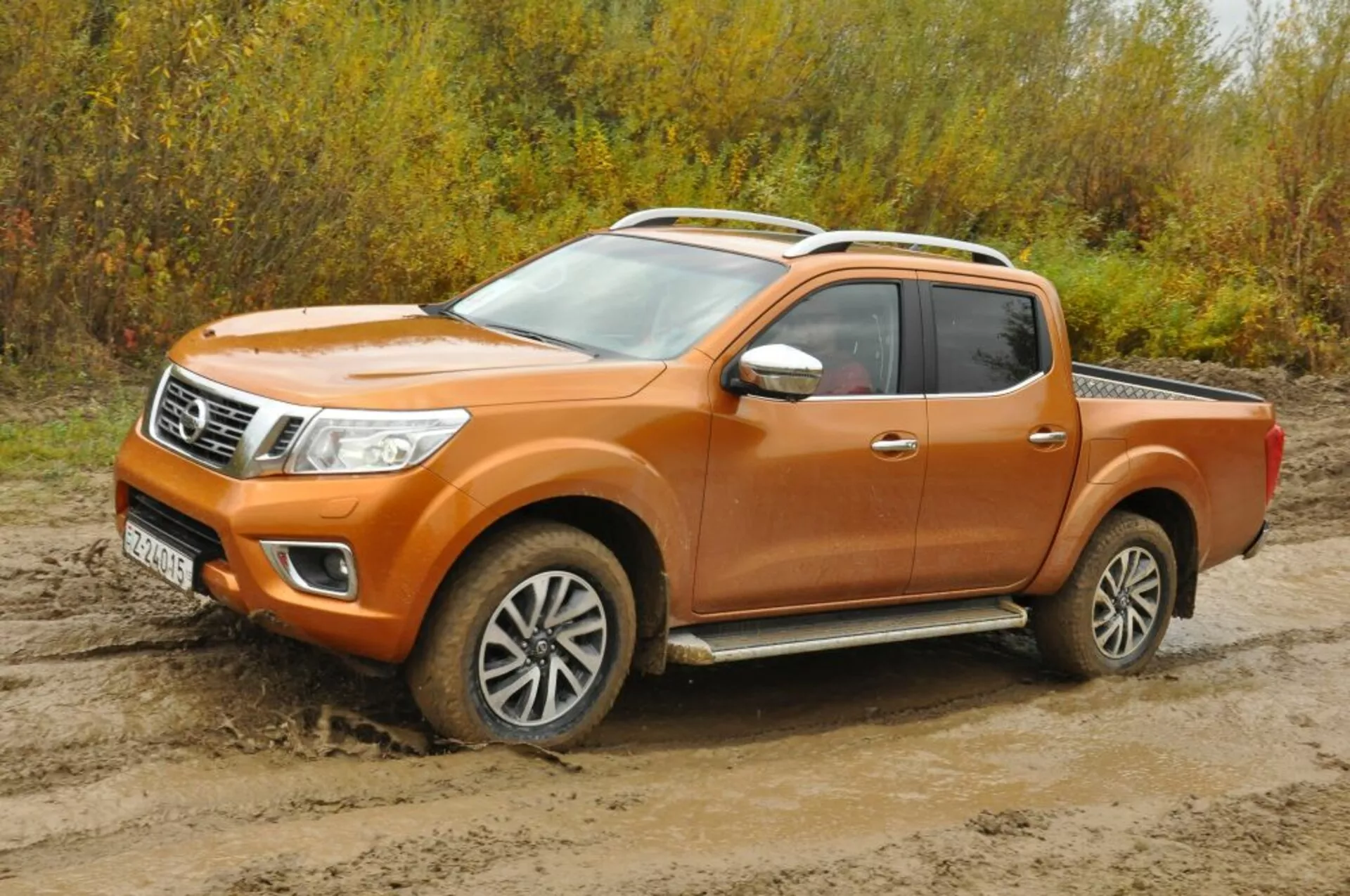 Oranžni pickup Nissan Navara letnik 2016 iz sprednjega pogleda pod kotom, ki prikazuje žaromete, rešetko s kromiranimi poudarki, lita platišča in konfiguracijo kabine za posadko na grobem terenu