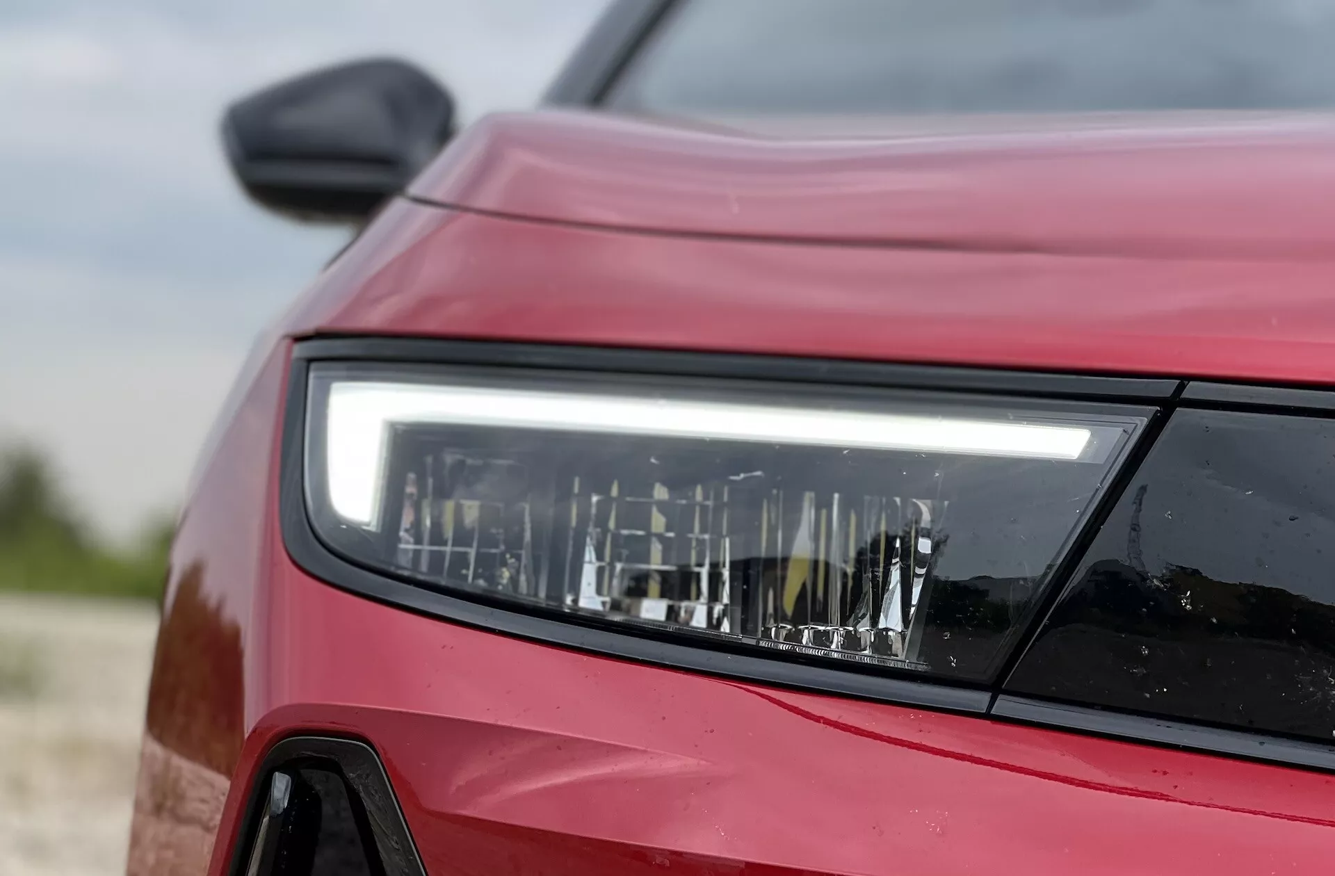 Podroben pogled s stranske sprednje perspektive na rdeči Opel Astra 2022 osredotočen na detajlni dizajn LED žarometa, ki prikazuje sodobno tehnologijo razsvetljave in oblike vozila