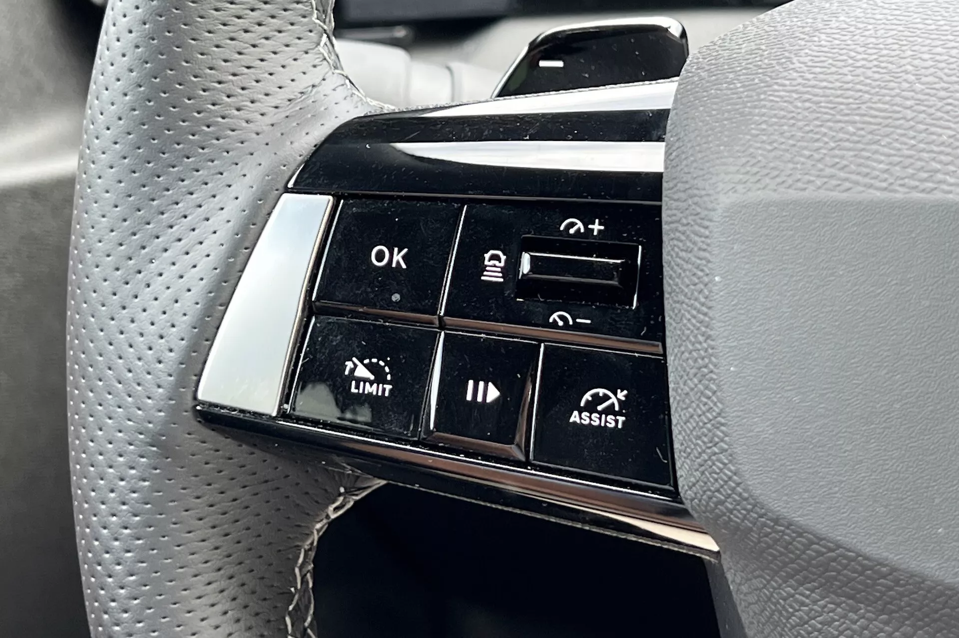 Podroben pogled na skupino gumbov na volanu Opel Astra 2022, ki poudarja napredne funkcije pomoči pri vožnji, vključno z adaptivnim tempomatom in pomočjo pri ohranjanju voznega pasu, s poudarkom na funkcionalnih oznakah, kot so OK, +, -, LIMIT in ASSIST iz perspektive voznika