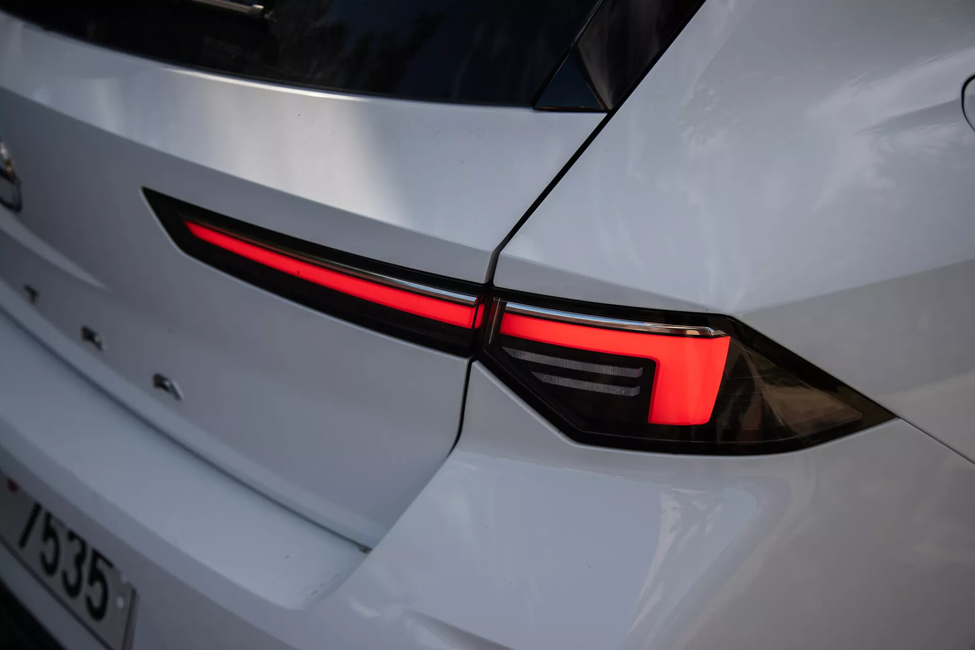 Posnetek leve zadnje luči Opel Astra 2022, ki prikazuje elegantno LED zasnovo in integracijo v belo karoserijo s športnim estetskim videzom