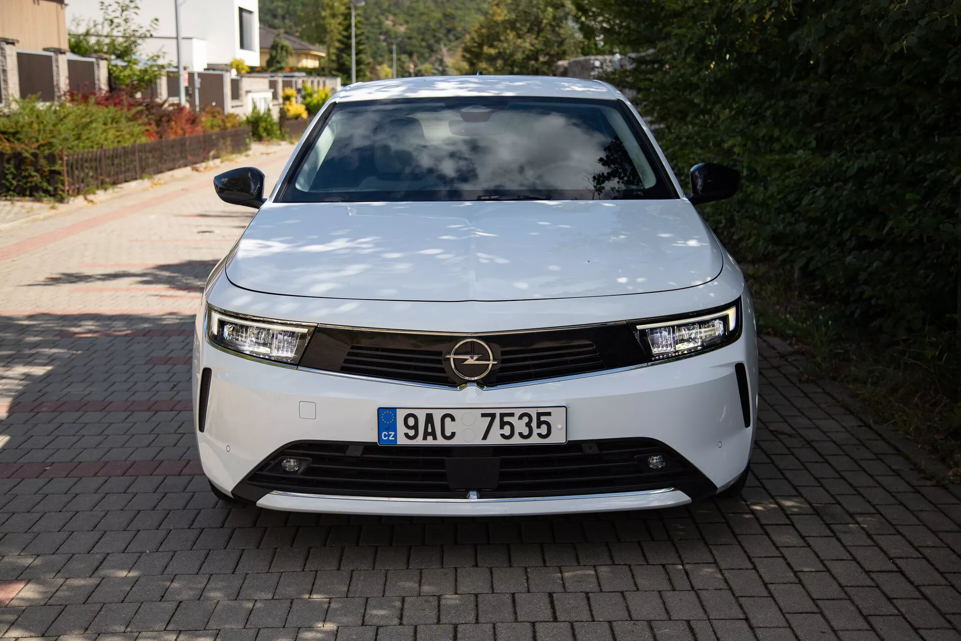 Sprednji pogled na Opel Astro 2022, ki prikazuje sodobno zasnovo električnega vozila z LED žarometi, dekorativno masko in aerodinamično obliko, parkirano na dovozni poti stanovanjske hiše