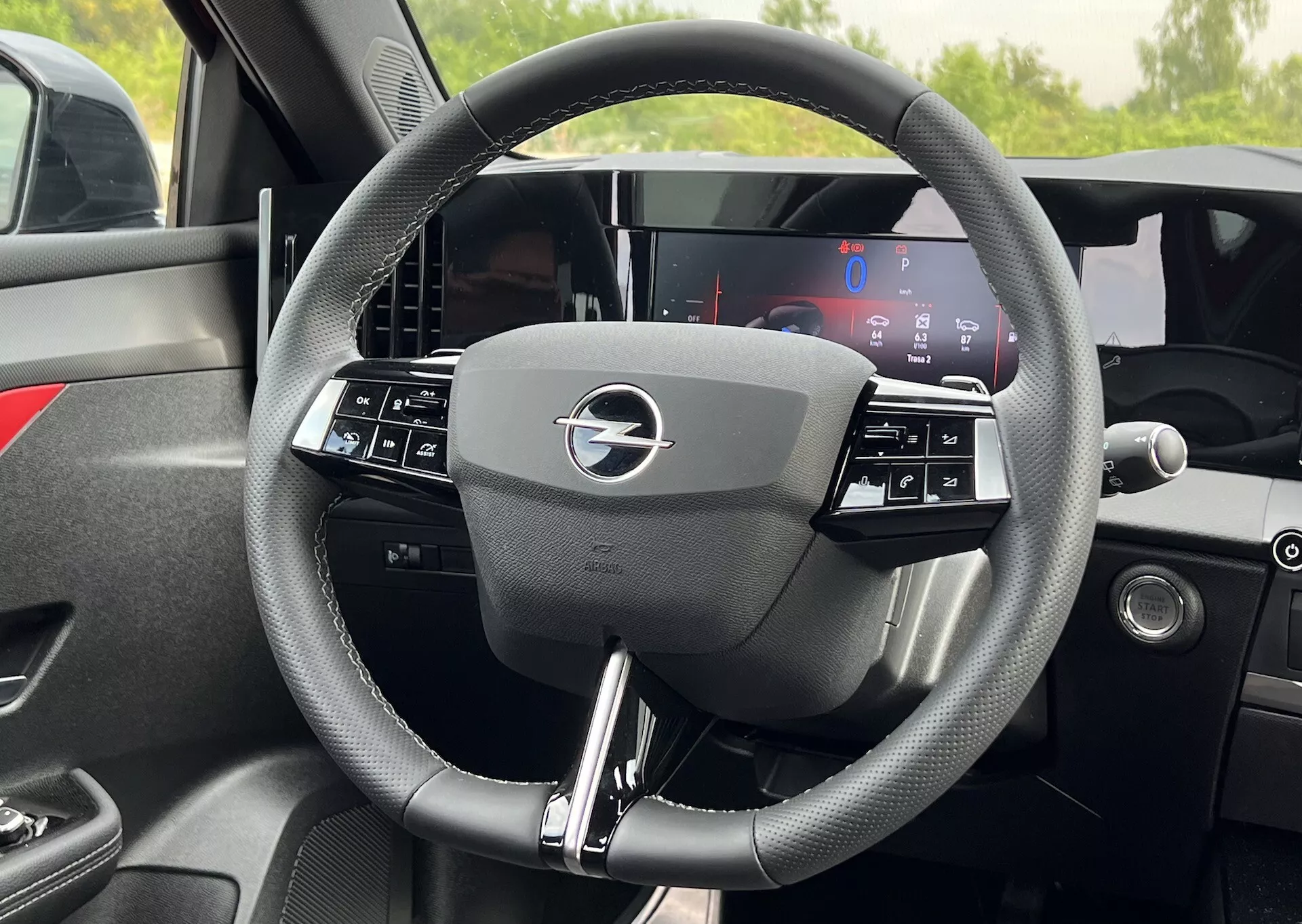 Podroben notranji pogled na volan Opel Astra 2022 s trokrakim dizajnom z integriranimi upravljalnimi gumbi in povsem digitalnim prikazovalnikom armaturne plošče za njim, ki poudarja sodobno tehnologijo vozil in ergonomijo