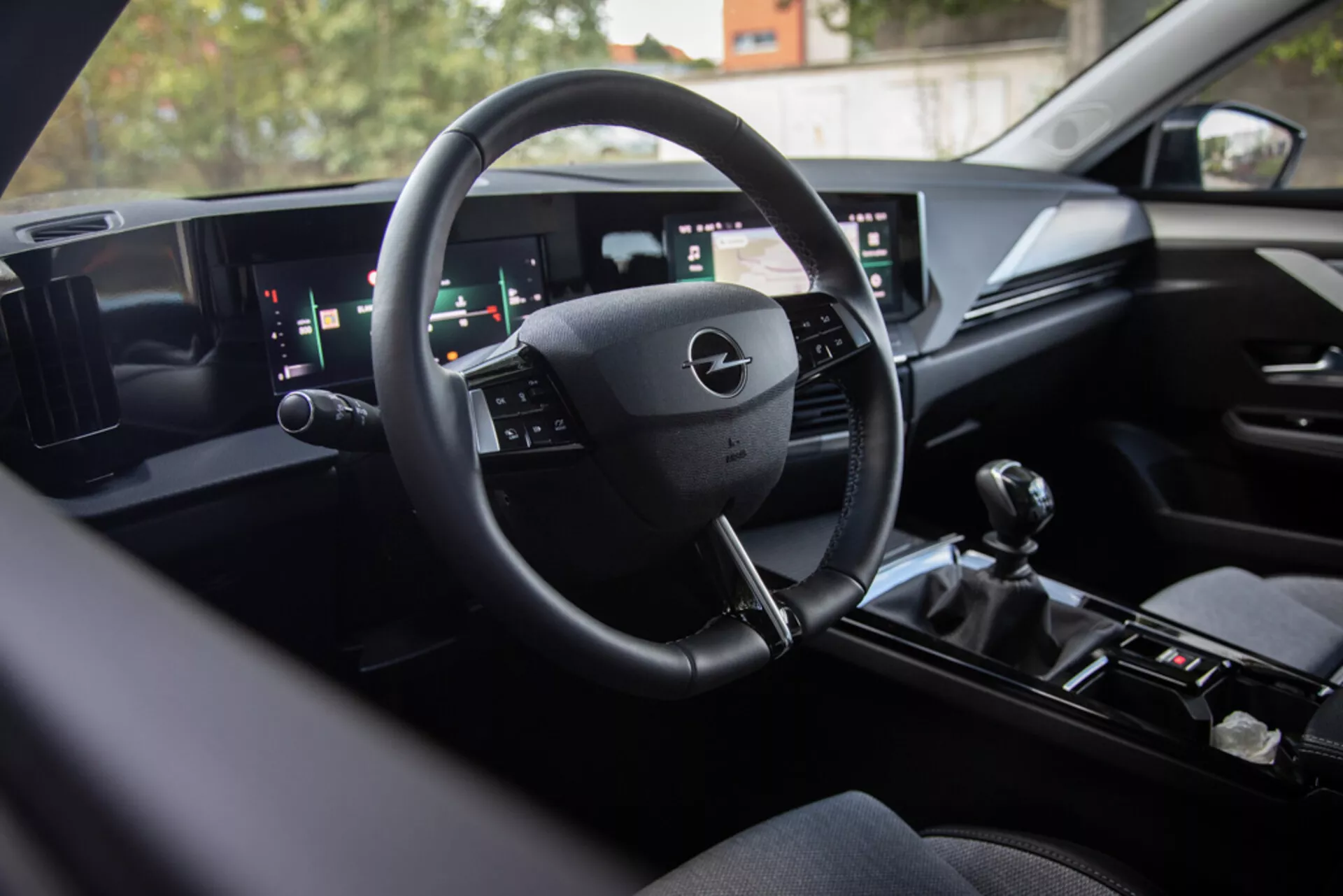 Notranjost Opel Astre 2022, ki prikazuje moderno tehnologijo digitalnih armaturnih plošč, multifunkcijski volan, širok sistem za informacije in zabavo z dvojnim zaslonom in ročno prestavno ročico za športne zmogljivosti, pogled s sedeža zadaj proti voznikovemu prostoru s premium zaključki