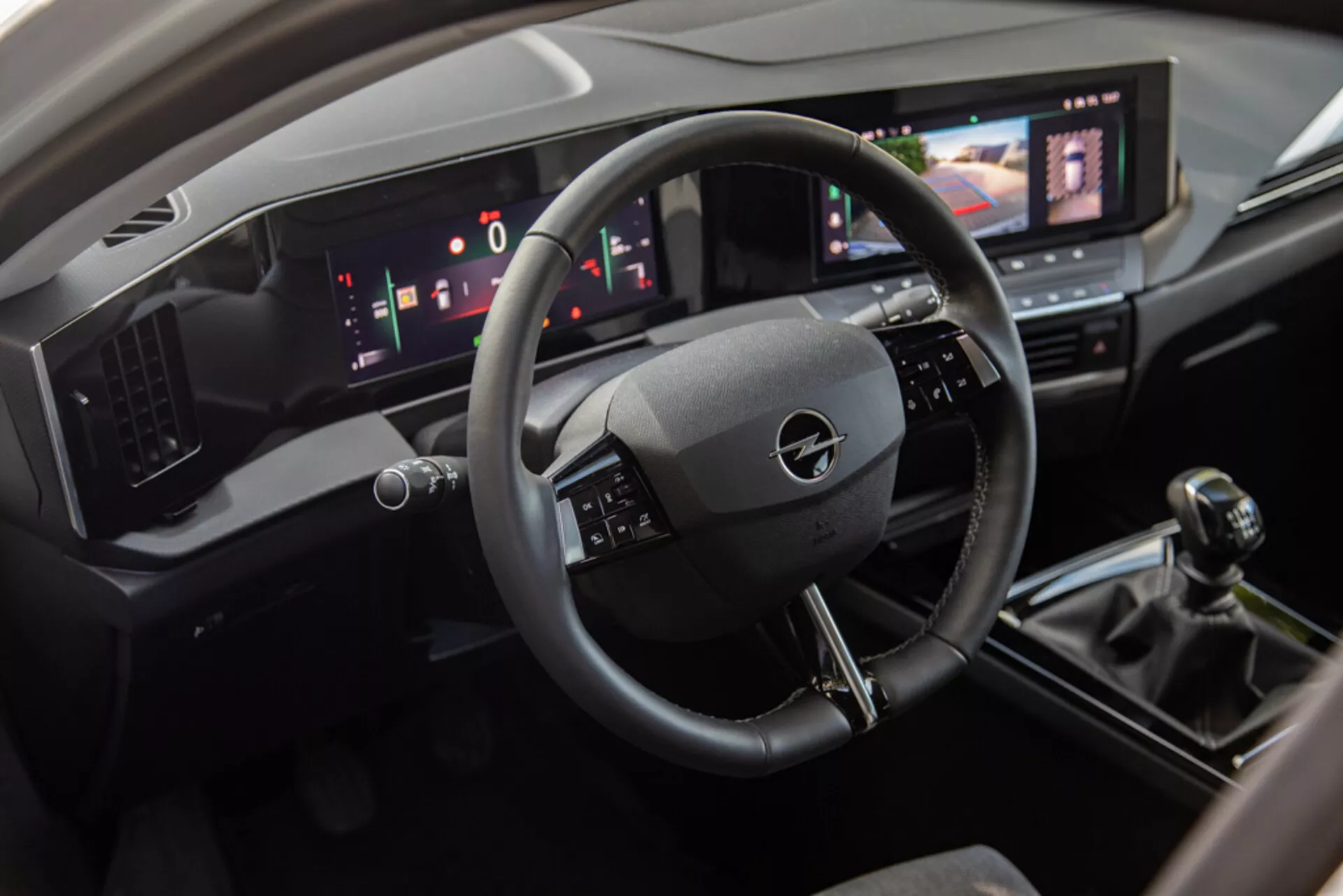 Notranjost Opel Astra 2022, ki prikazuje voznikov prostor s tridelno volansko obročko, digitalno armaturno ploščo in centralno konzolo vključno z zaslonom na dotik za informacijsko-zabavni sistem, ročni menjalnik in sodobne nadzorne elemente za klimatizacijo