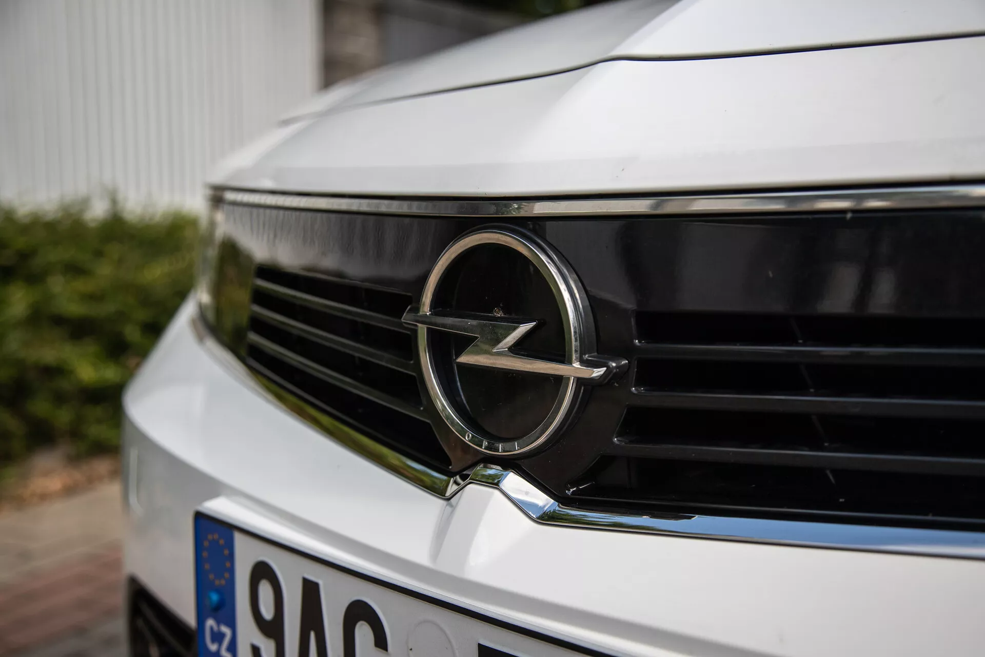 Posnetek od blizu sprednjega žara in značke Opel modela 2022, ki prikazuje detajle emblem in horizontalno zasnovo rešetk iz nizkega, rahlo izcentričnega kota, poudarja sodobno estetiko in identiteto blagovne znamke avtomobila