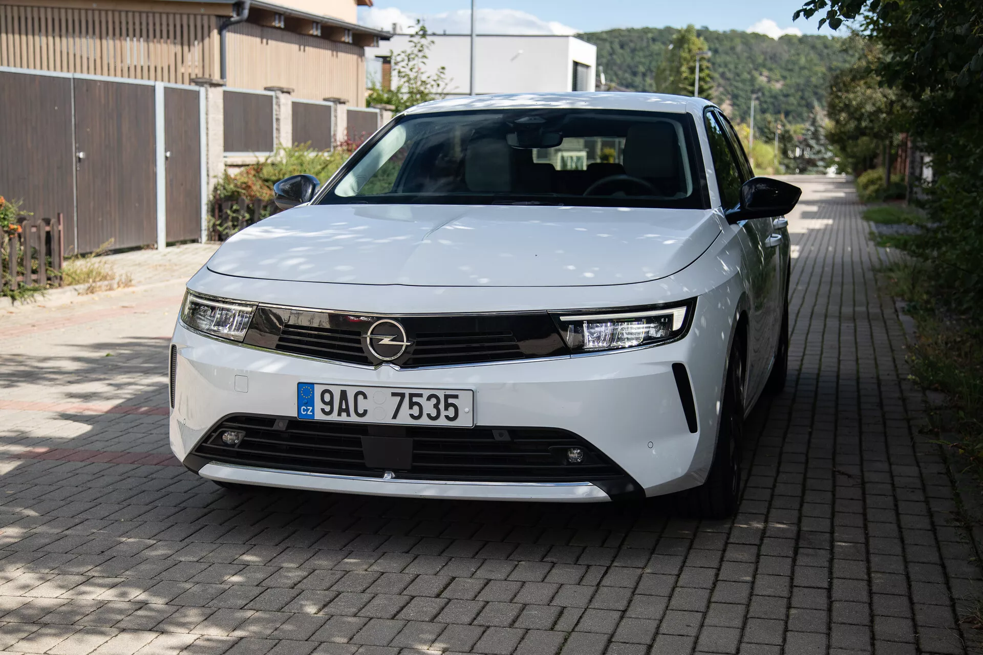 Prednji tričetrtinski pogled na Opel Astra 2022 z LED žarometi, minimalističnim dizajnom rešetke, delno vidnimi litoželeznimi kolesi in elegantnimi karoserijskimi ploščami na evropski stanovanjski ulici