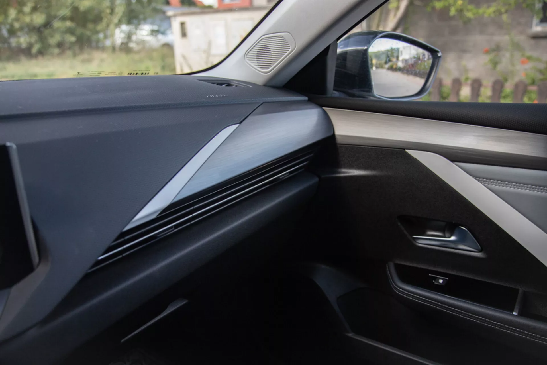 Notranji pogled iz perspektive sovoznikovega sedeža prikazuje oblikovanje armaturne plošče, obrobe in vratnega panela v Opel Astra 2022, s temnimi, elegantnimi konturami, osredotočenimi na teksturo materiala in morebitne tehnološke integracije