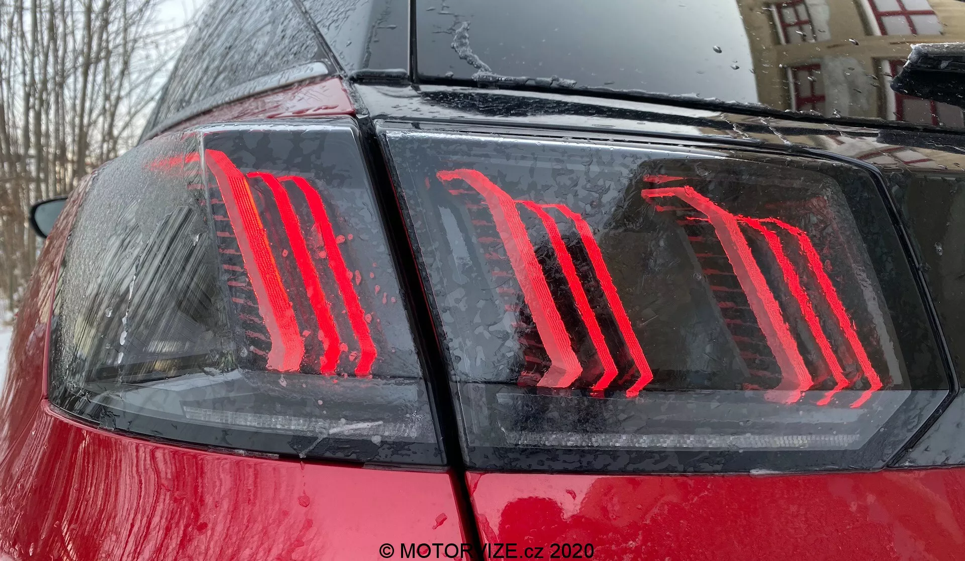 Bližnji pogled zadnjega dela avtomobila Peugeot 3008 iz leta 2021, ki poudarja sodobno, navpično osvetljeno LED zadnjo luč na sijoči rdeči karoseriji z vodnimi kapljicami, kar kaže na zunanji prostor med ali po dežju; zadnja luč uporablja energetsko učinkovito tehnologijo in služi kot zavorna in dnevna luč.
