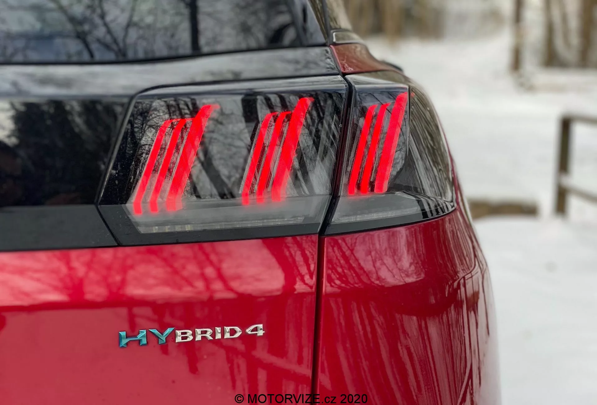 Peugeot 3008 Hybrid4 2021 - Bližnji pogled z levega zadnjega kota, ki prikazuje živahno rdečo barvo, moderni rdeči LED sestav zadnjih luči z razločnimi navpičnimi segmenti, pokrov prtljažnika in hibridno oznako na zadnjem levem kotu, kar označuje hibridni pogonski sistem z možno zmogljivostjo štirikolesnega pogona.
