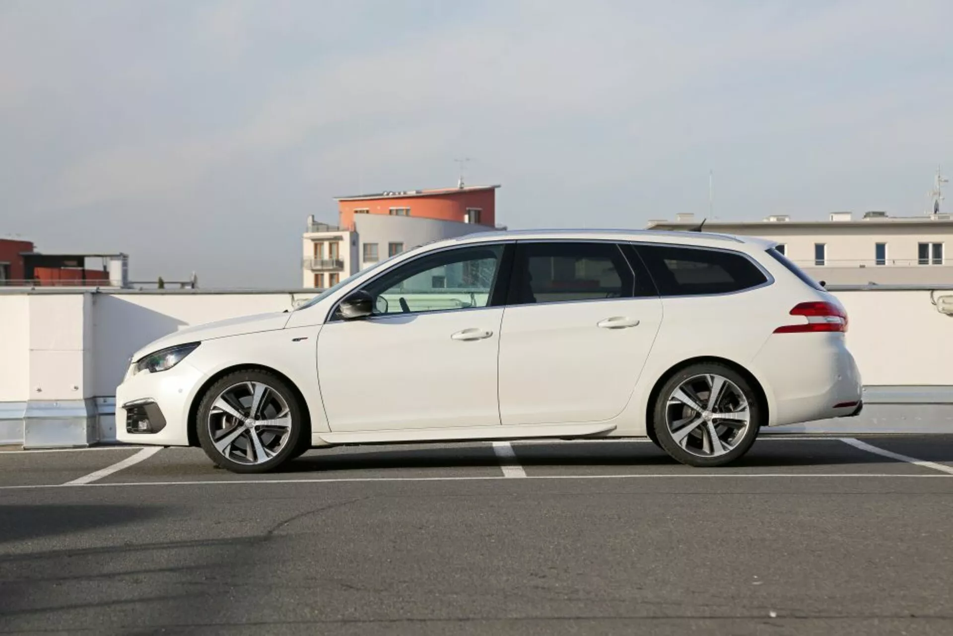 Beli karavan Peugeot 3008 letnik 2016 parkiran na parkirišču na prostem, prikazuje elegantne žaromete, stranska ogledala z integrirano tehnologijo, zatemnjena okna, lita platišča s petimi kraki in spojler na strehi za izboljšano aerodinamiko pod jasno dnevno svetlobo