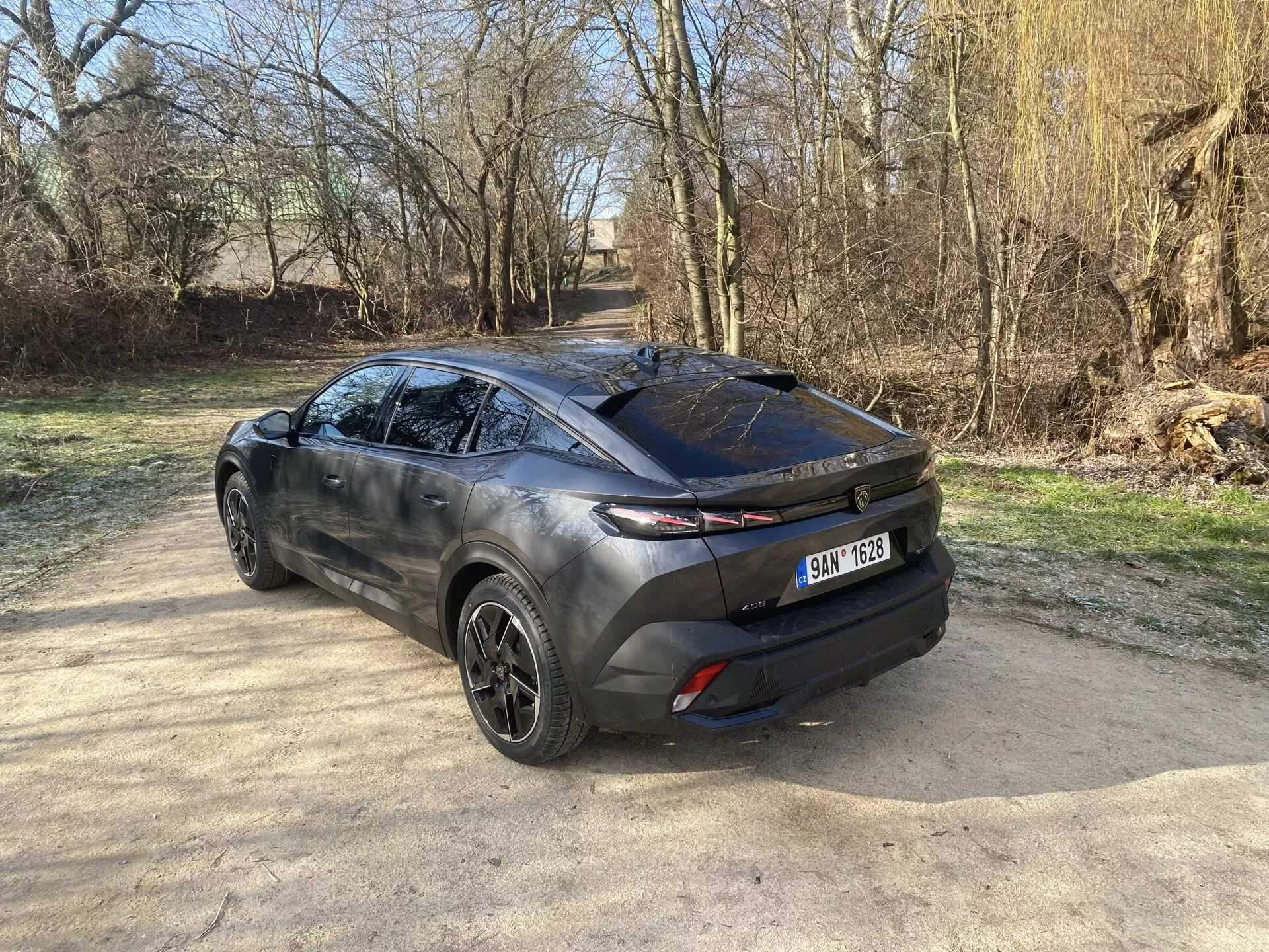 Zadnji tričetrtinski pogled na Peugeot 408 2023, ki prikazuje njegov sodoben crossover dizajn, poudarja zadnja vrata, elegantno zadnje okno in horizontalne zadnje luči, razširjene v stransko karoserijo, z vpogledom v zlitinska kolesa, kiparski stranski profil in dvobarvno zunanjo podobo pod naravno sončno svetlobo
