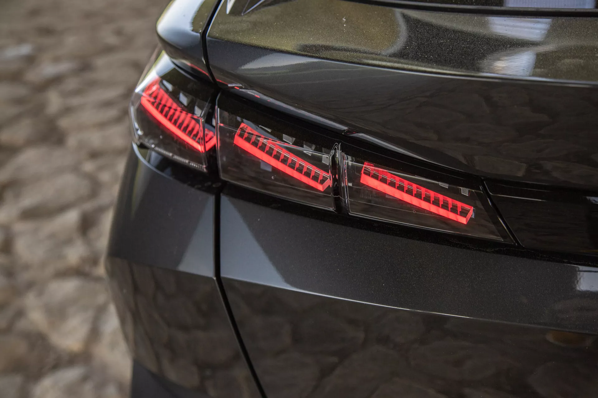 Podroben pogled na sijoče črne zadnje luči Peugeota 408 letnik 2023, z modernimi LED elementi in elegantnimi dizajnimi poudarki, posnetimi iz rahlo dvignjenega kota