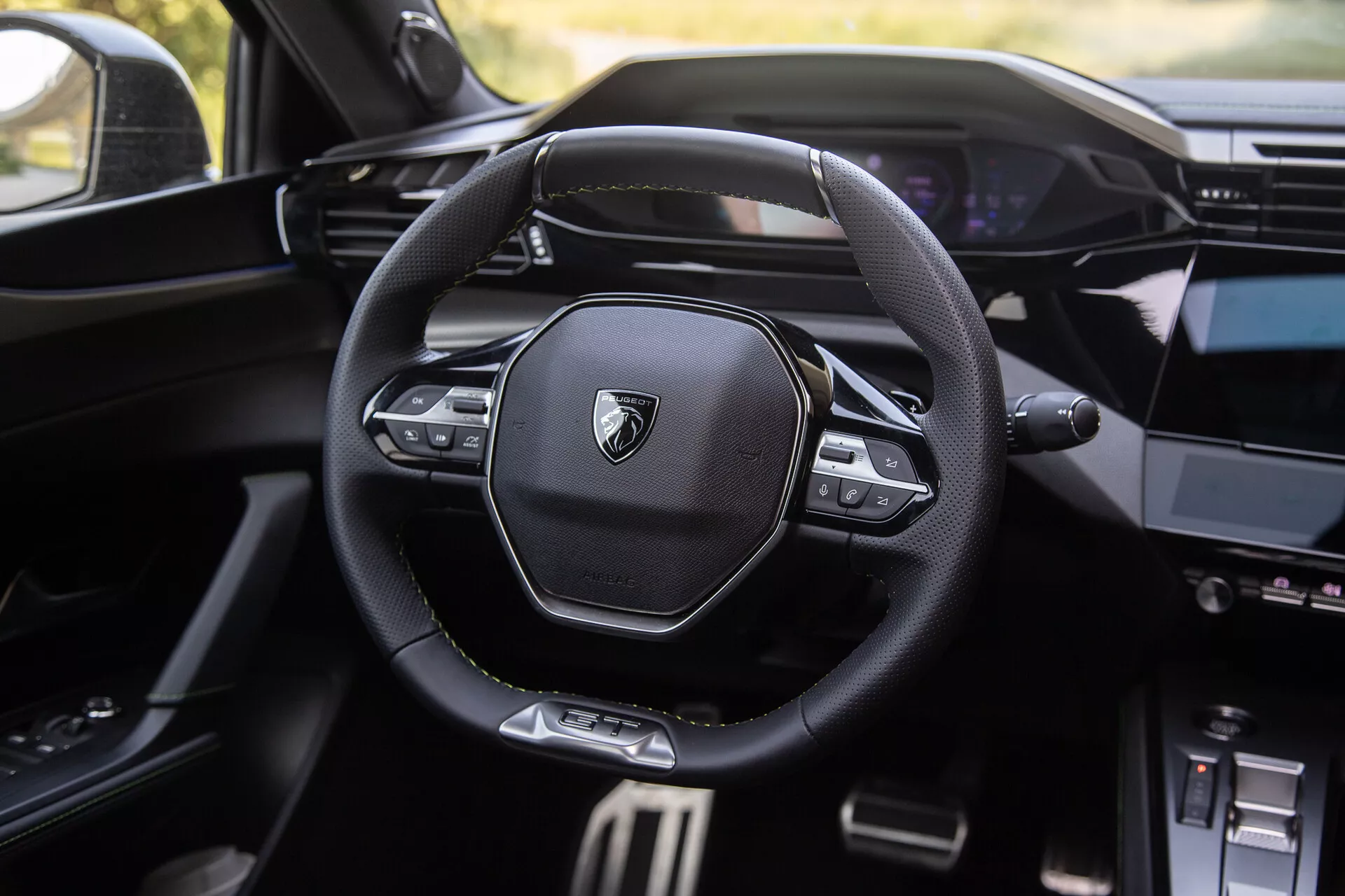 Notranjost Peugeota 408 letnik 2023 z modernim večfunkcijskim volanom z logotipom znamke, digitalno armaturno ploščo v ozadju in delno vidno sredinsko konzolo z informacijsko-zabavnim sistemom