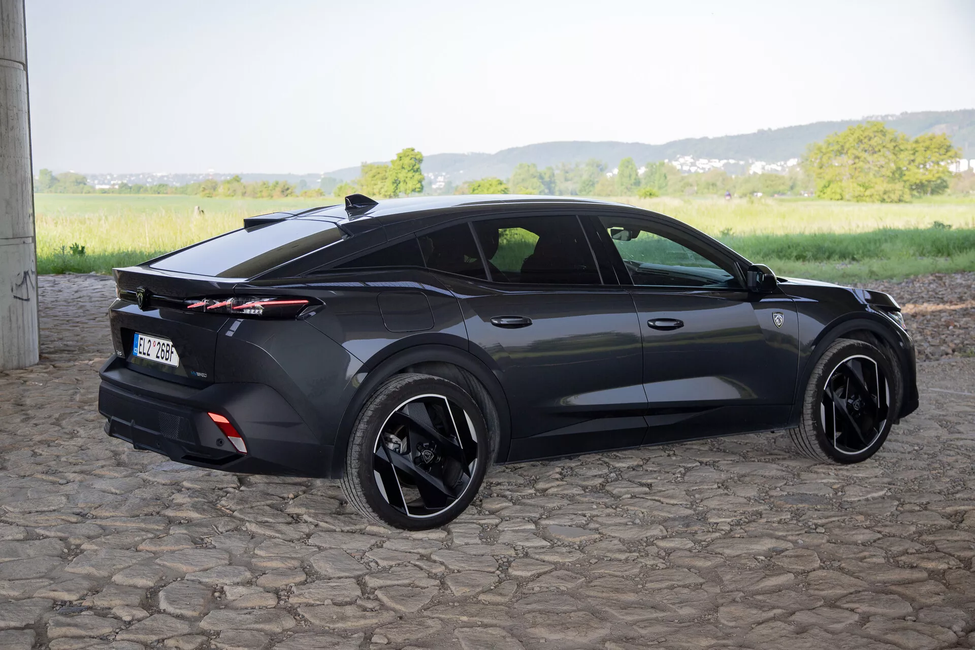 Peugeot 408 leta 2023, posnet z zadnjega kota tri četrt, ki poudarja njegov športni hatchback dizajn, integrirani zadnji spojler s celotrajnimi zadnjimi lučmi, črna lita platišča in sodobne značilnosti kot so vratne kljuke v ravnini z vrati in stranska ogledala z vgrajenimi smerniki, v naravni dnevni svetlobi