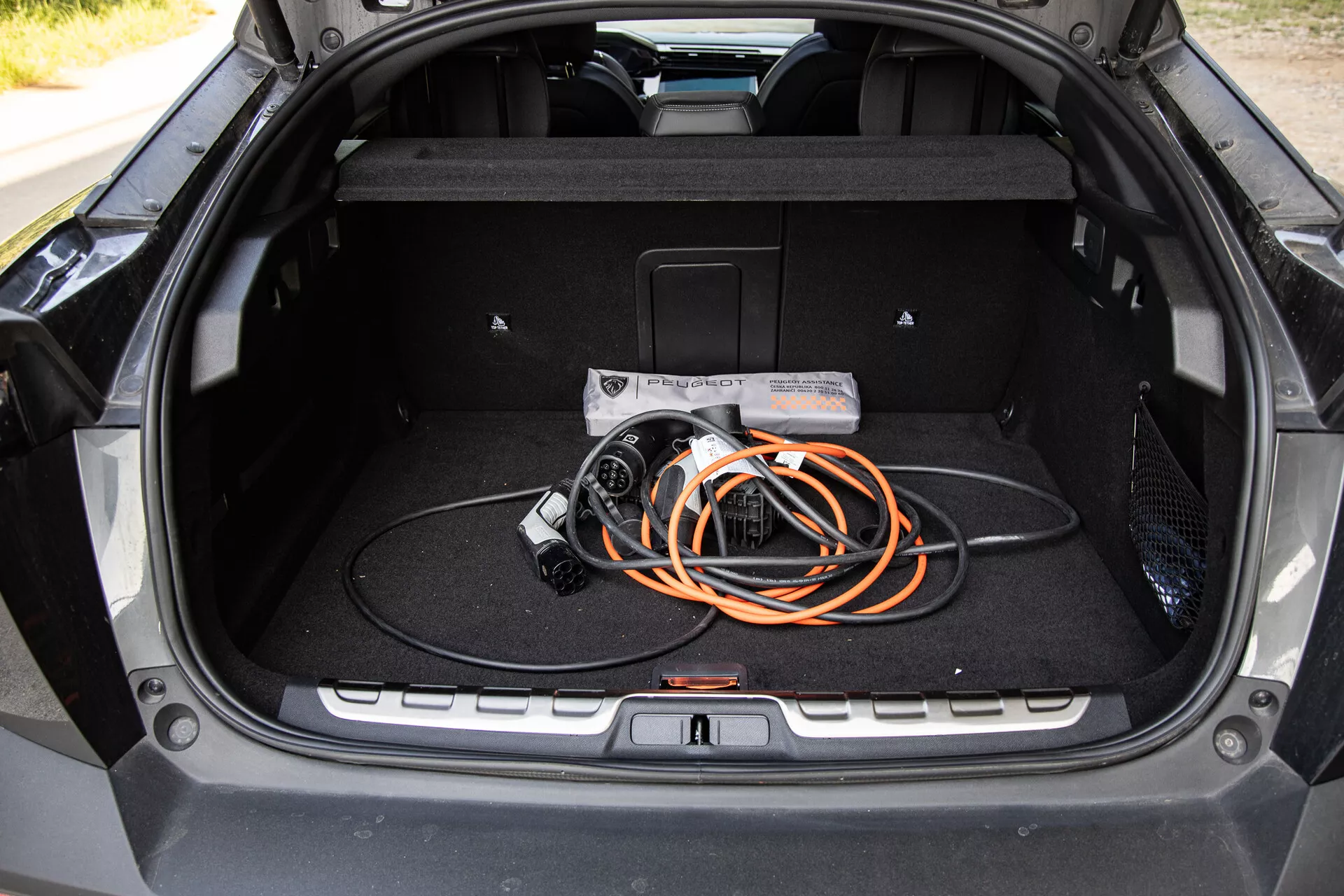 Notranjost prtljažnika Peugeot 408 2023, ki prikazuje prostorno zasnovo in kabel za polnjenje električnih vozil, poudarjajoč tehnologijo EV in sodobno kakovost izdelave.
