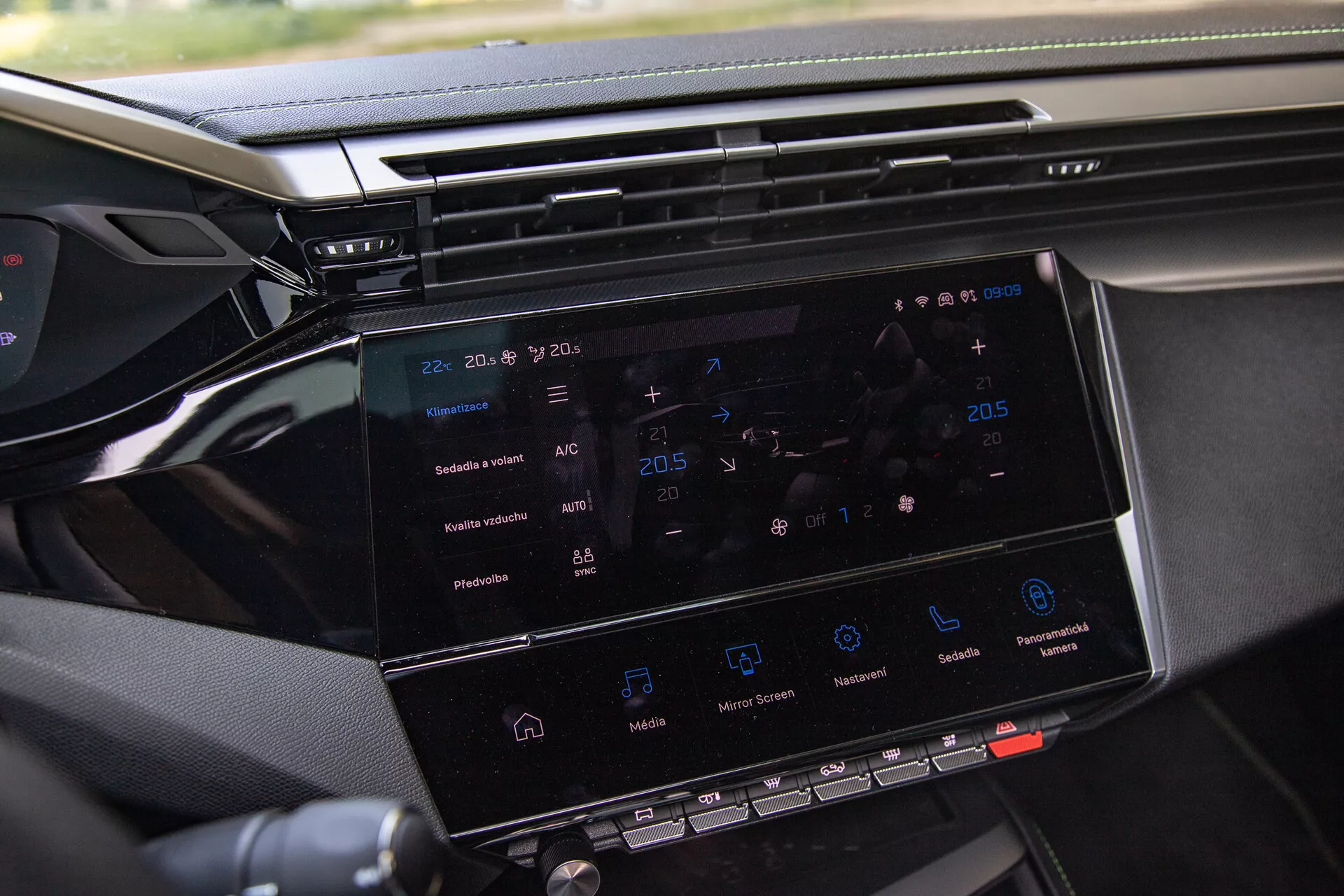 Posnetek iz bližine infotainment sistema Peugeot 408 2023, ki prikazuje 8-10 palčni zaslon na dotik z navigacijo, nadzorom klime, ikonami za predvajanje medijev in pogledom na armaturno ploščo, posneto s strani sovoznika