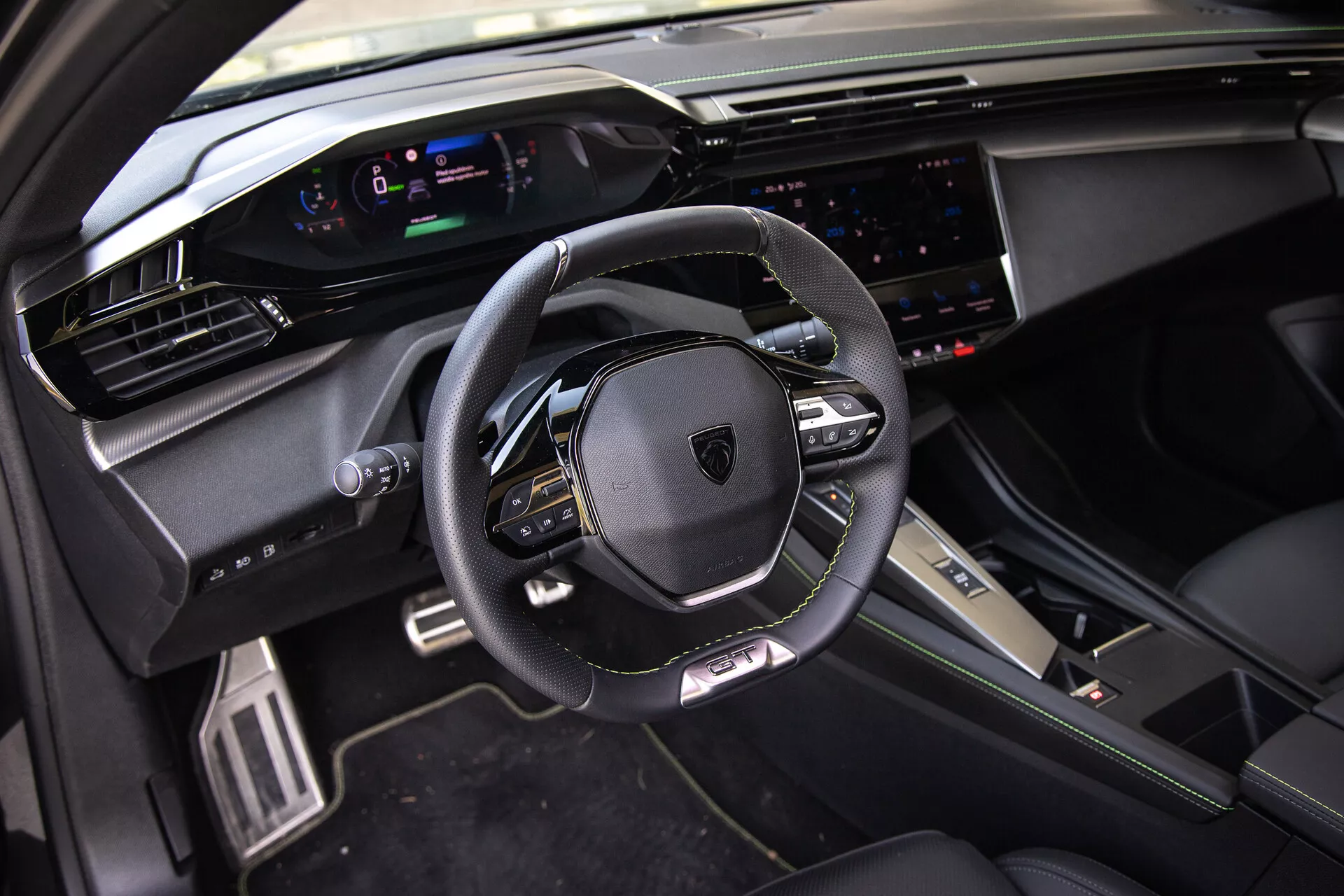Notranjost Peugeota 408 iz leta 2023 z usnjenim, večfunkcijskim volanom, digitalnim instrumentnim sklopom, širokim zaslonom na dotik infotainment sistema in športnimi, premium oblikovalskimi elementi pod naravno dnevno svetlobo iz perspektive sovoznika spredaj.