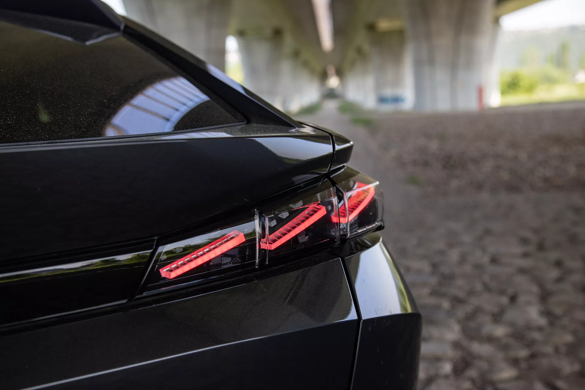 Podroben posnetek zadnjega dela Peugeota 408 iz leta 2023 z LED zadnjo lučjo, elegantnim dizajnom prtljažnika z vgrajenim spojlerjem in sijajnim črnim zaključkom pod strukturirano senco
