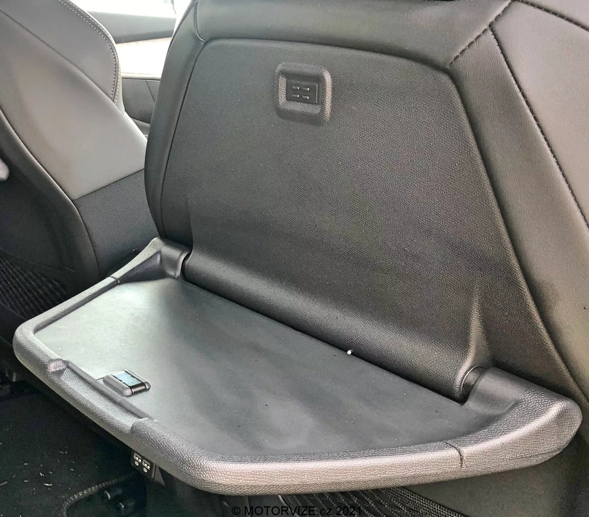 Notranji pogled na Peugeot 5008 2021 s zadnjim sedežem, ki ima zložljiv naslon za roke ali mizico, z mešanico tkanine in usnjene oblazinjene ter z vgrajenim zaslonom ali kontrolno ploščo na zadnji strani naslona za glavo sprednjega sedeža.