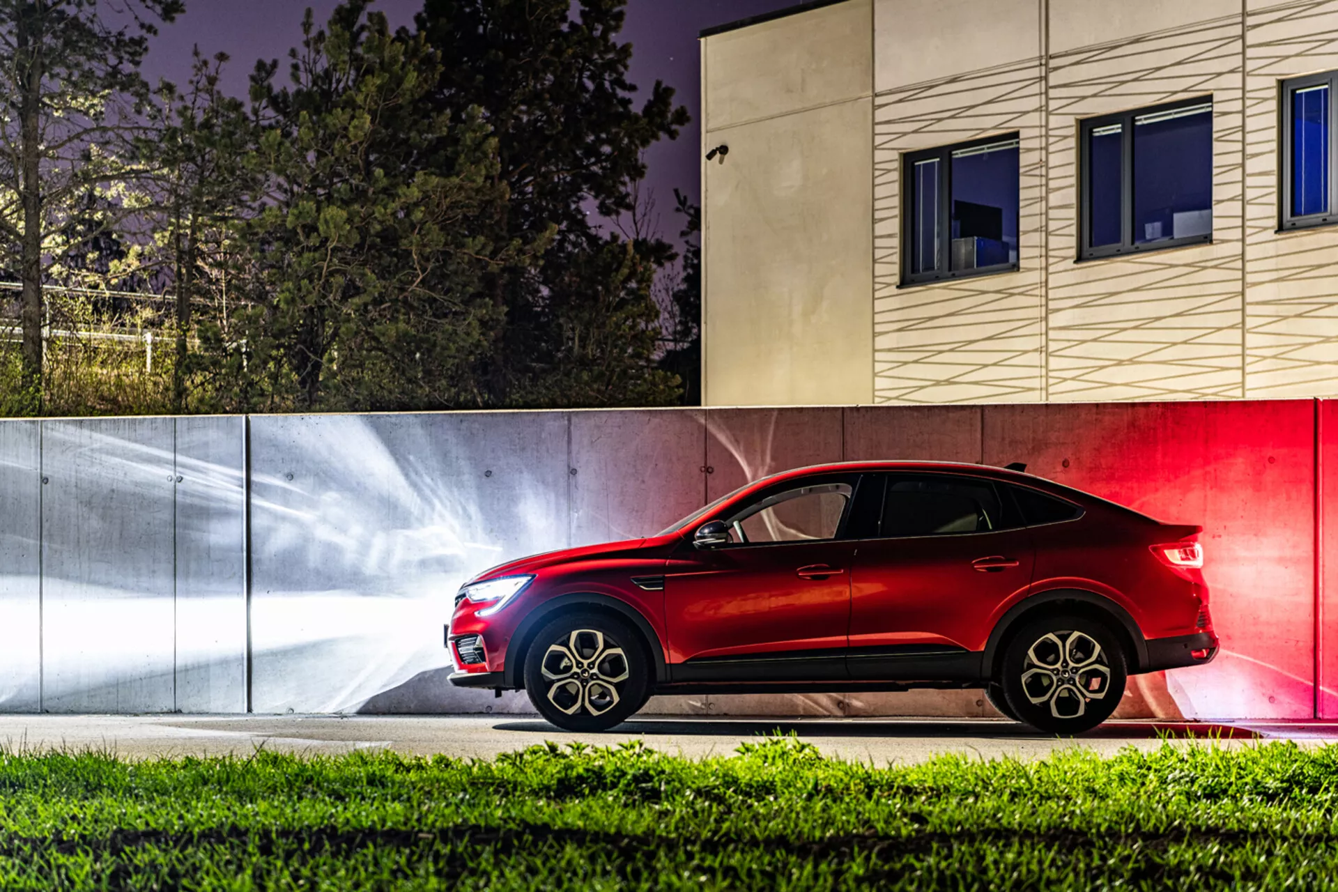 Bočni pogled na Renault Arkana 2021 ponoči z dinamičnimi svetlobnimi sledi in sodobnim urbanskim ozadjem, ki prikazuje njegov eleganten dizajn SUVja podobnega kupéju in napredno tehnologijo razsvetljave.