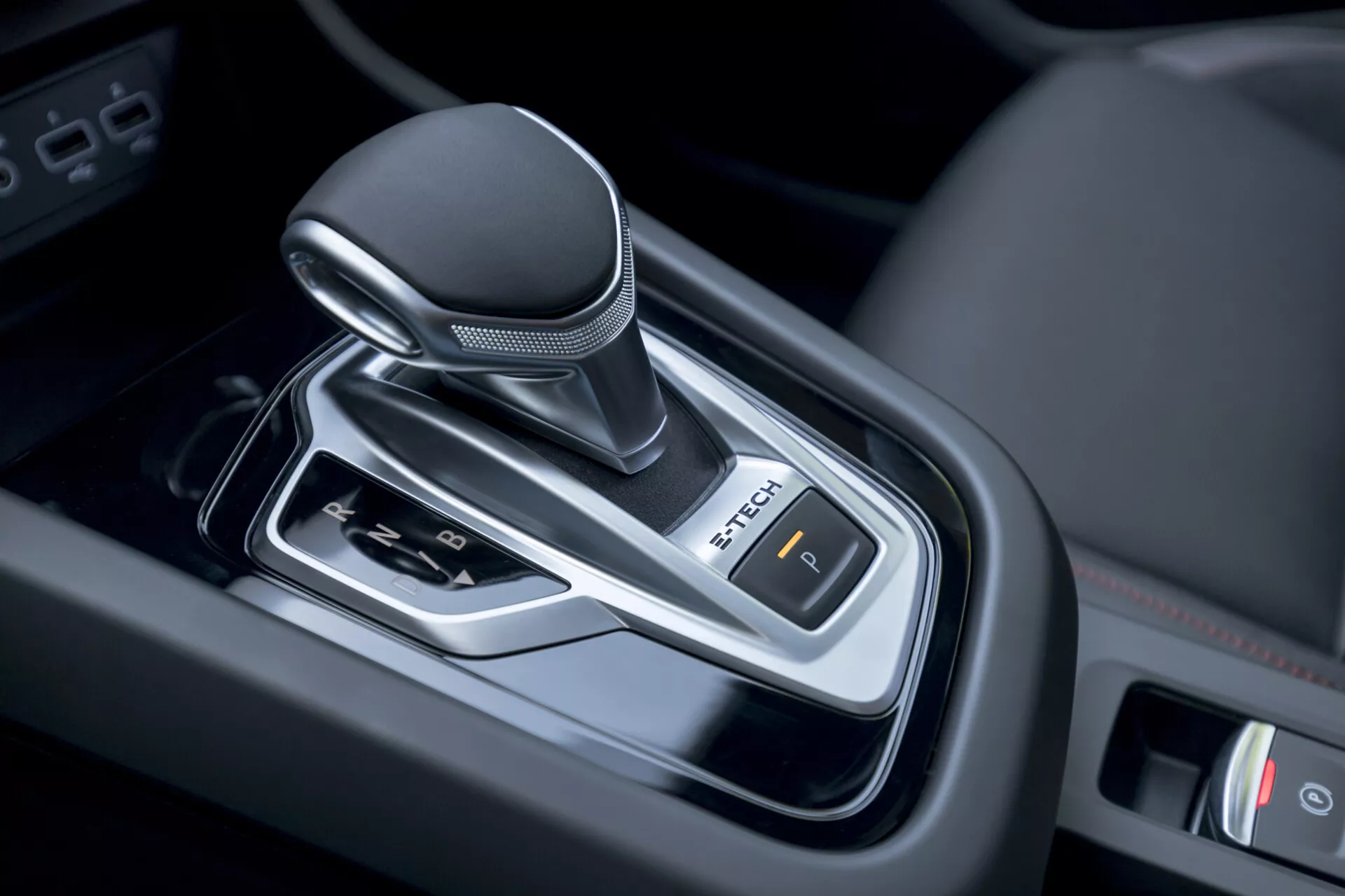 Pogled od blizu na ročico za avtomatski menjalnik Renault Arkana 2021 v notranjosti vozila, ki prikazuje sodobno zasnovo z ročajem, ovitim v usnje, kromiranimi poudarki in nadzorom elektronske parkirne zavore.