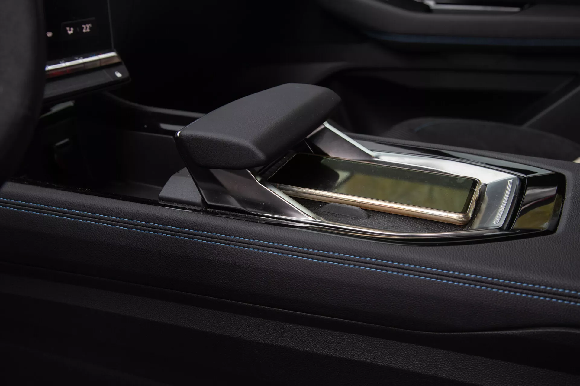 Podroben pogled na razkošno sredinsko konzolo Renault Austral 2022 z moderno avtomatsko prestavno ročico, ki predstavlja ergonomično zasnovo z usnjenimi in kromiranimi poudarki, postavljeno proti visokosijajnemu črnemu okrasju in sofisticiranemu vmesniku za nadzor zabaviščnega sistema.