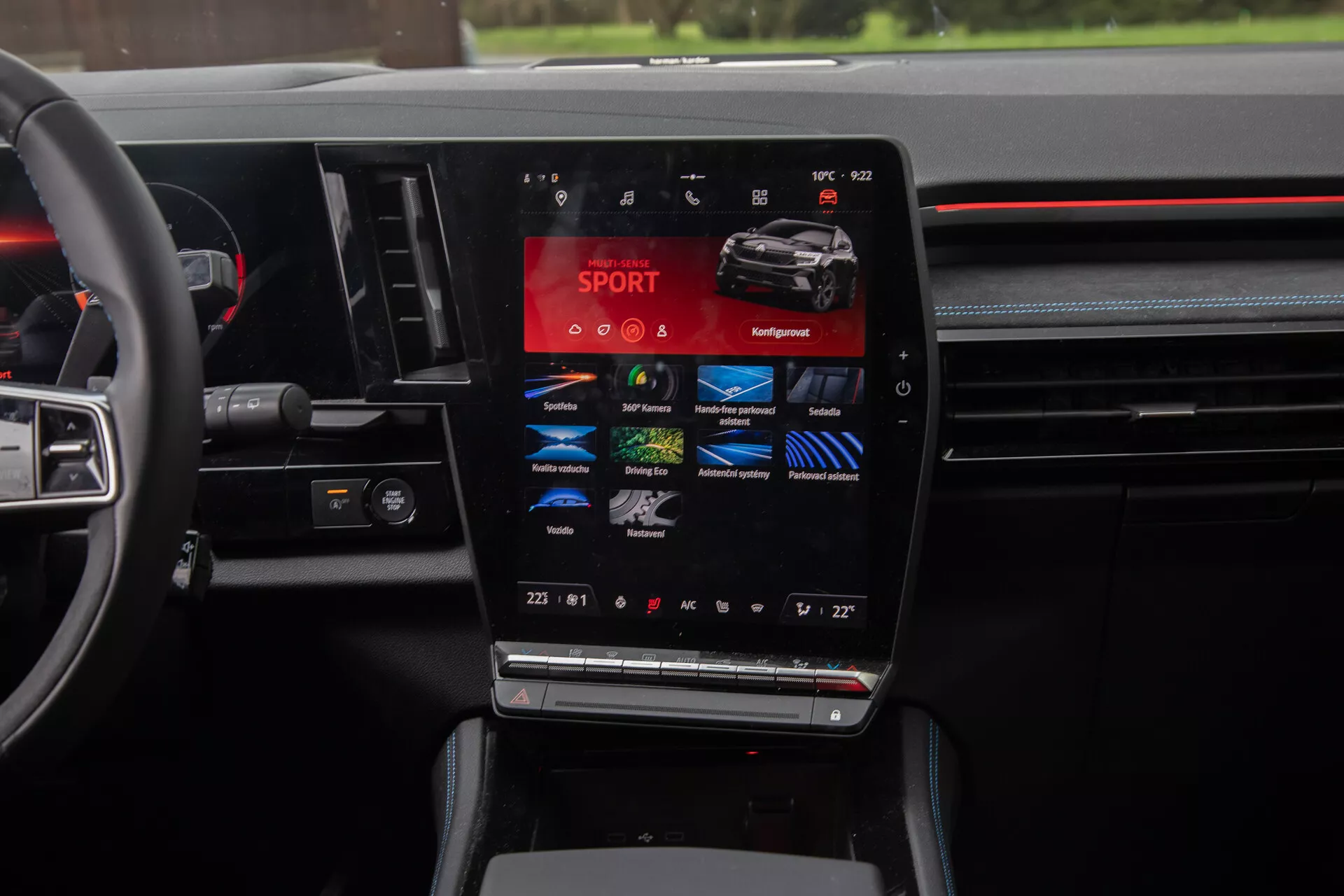 Pogled na notranjost Renault Austral 2022, ki poudarja sredinsko konzolo z velikim vertikalnim zaslonom na dotik, ki prikazuje vozne načine, kot so SPORT, Comfort, Eco, skupaj z nastavitvami dvoconega klimatskega nadzora in večfunkcijskih krmilnih gumbov na volanu, kar zajema bistvo sodobne tehnologije avtomobilov in luksuzne oblike.
