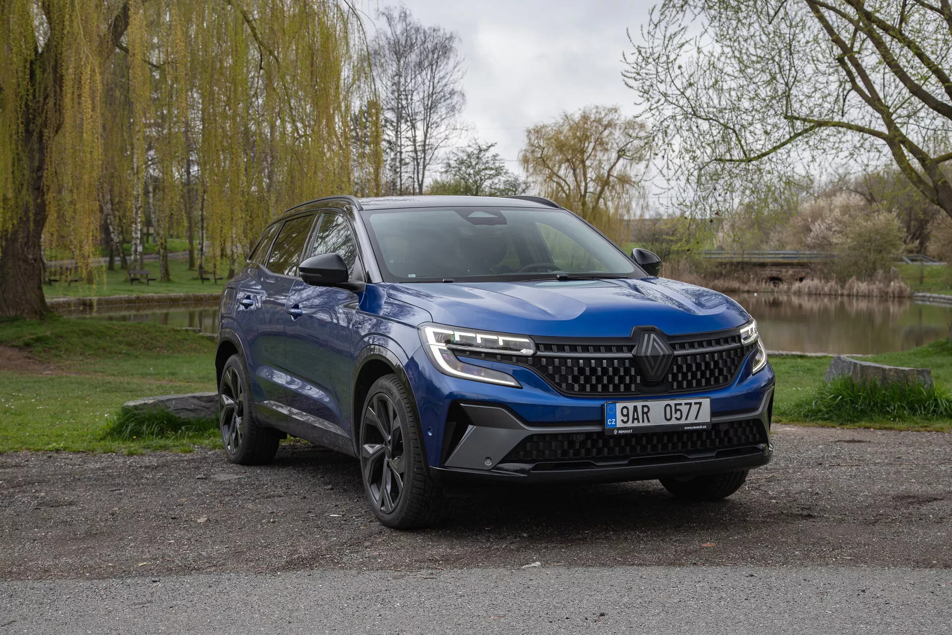 Modri SUV Renault Austral 2022, parkiran na prostem, prikazuje sprednji del in stran voznika z LED žarometi, športnim odbijačem in aluminijastimi kolesi ob naravnem ozadju