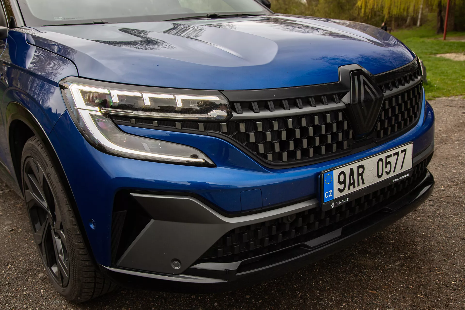 Podrobni pogled na Renault Austral 2022, ki prikazuje elegantne LED žaromete, dinamično zasnovo maske in podrobno oblikovanje sprednjega odbijača in kolesa, kar poudarja sodobno estetiko in tehnologijo vozila.