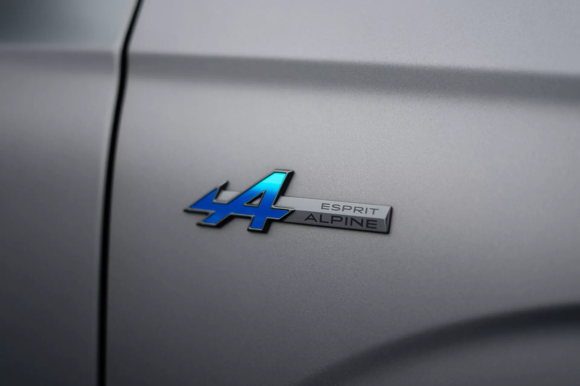 Podrobna slika emblema Alpine pri Renault Austral 2022 z oznako modela 'ALPINE ESPRIT' na kovinsko modri in kromirani površini, posneta pod kotom za plitko globino polja