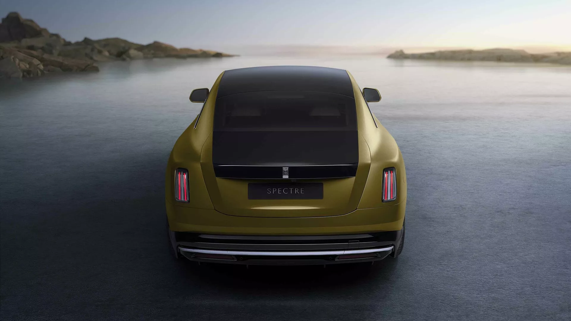 Rolls-Royce Spectre 1. generacija 2023 v metalik zlati barvi, posnet iz zadnjega zornega kota ob zlati uri, poudarja njegove LED zadnje luči, aerodinamično obliko prtljažnika, poliran zadnji odbijač, dvojni izpušni sistem in postavljen pred mirno obalno ozadje.