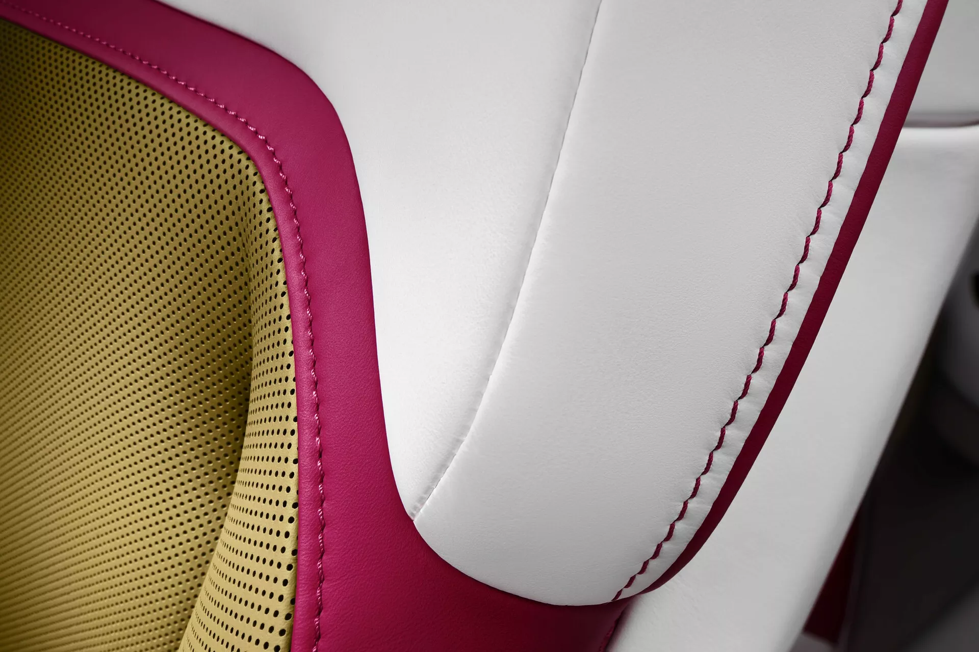 Podroben posnetek sedeža Rolls-Royce Spectre 2023, ki prikazuje oblazinjenje iz visokokakovostnega usnja v dveh tonih, rdeče kontrastno šivanje in vzorec satovja za zračnost in udobje, kar uteleša razkošje in obrtništvo.