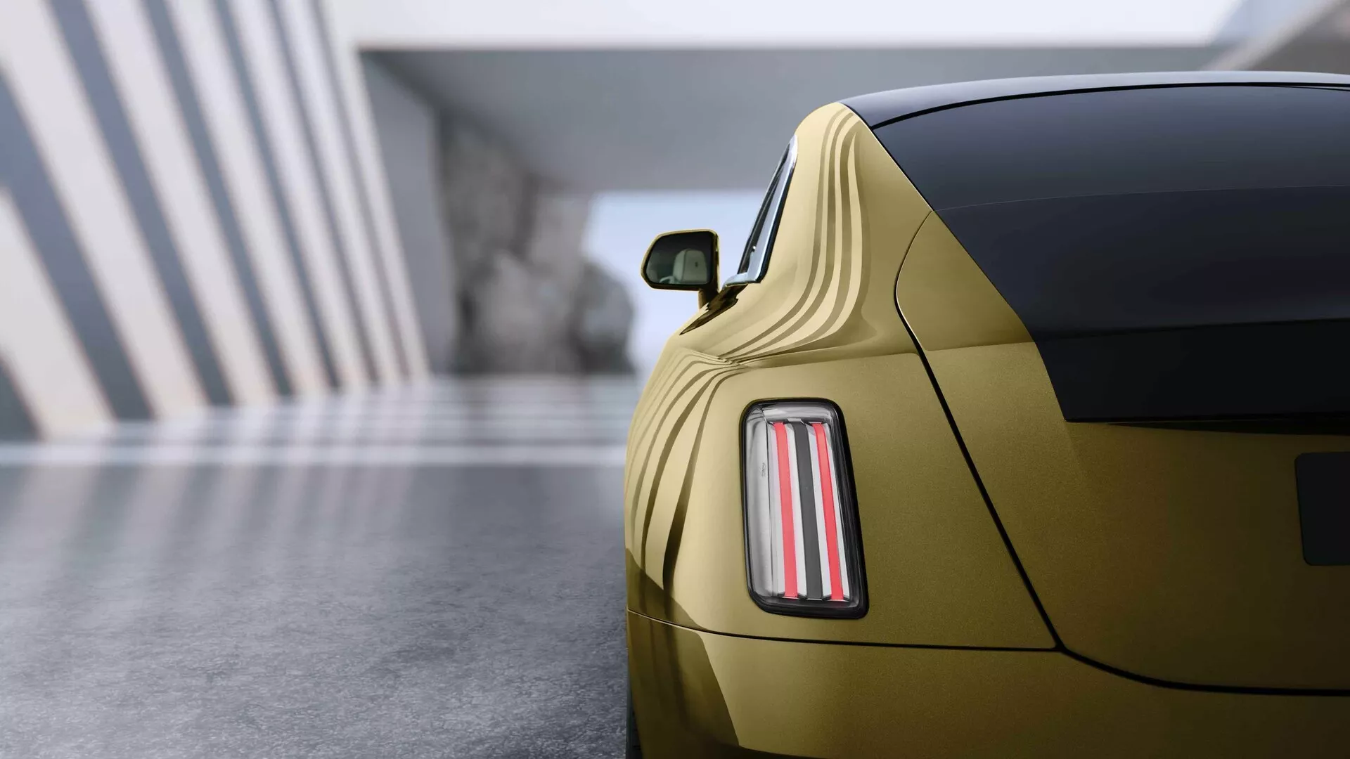 Rolls-Royce Spectre 2023, 1. generacija, prikazan iz zadnjega kota, ki poudarja sofisticirano zasnovo LED zadnjih luči, metalik zlato barvo in športni profil kupe v razstavnem prostoru