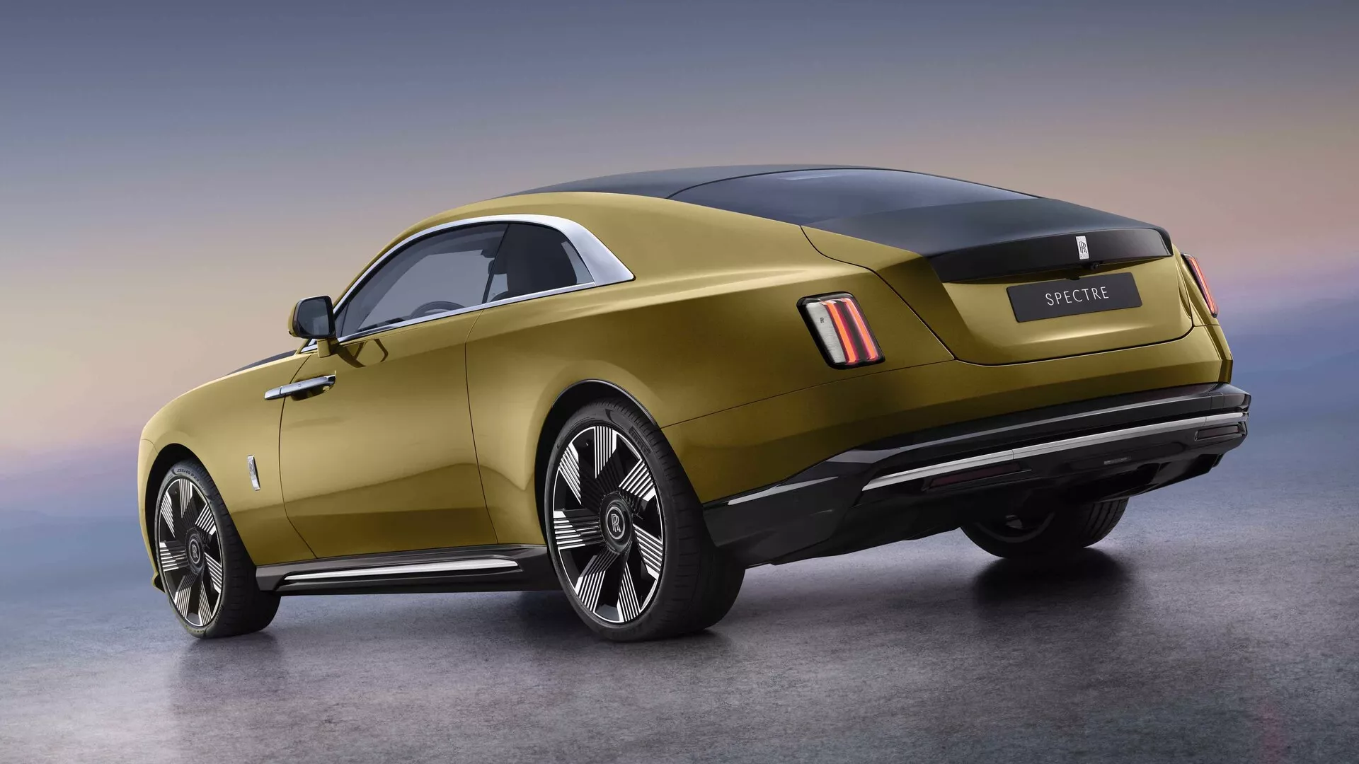 Zadnji tričetrtinski pogled na Rolls-Royce Spectre 2023, ki prikazuje velike zlitine platišč, sodobne LED zadnje luči, senzorje za pomoč pri parkiranju, dvojni izpušni sistem, značilno linijo ramen s kromiranimi poudarki, integriran zadnji spojler in panoramsko stekleno streho na gradientnem ozadju, kar uteleša razkošje in zmogljivost.