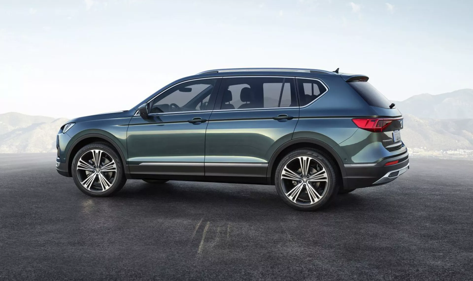 SUV Seat Tarraco 2019 prikazuje svoj bočni zadnji kot, prikazuje velika večkraka lita platišča, oblikovanje s štirimi vrati, elegantna bočna okna z majhnim aerodinamičnim zadnjim oknom, nežno padajočo streho z integriranim spojlerjem, obkrožajoče LED zadnje luči, metalik lak z zunanjimi kromiranimi okraski, ki poudarjajo njegov sodoben in vsestranski dizajn