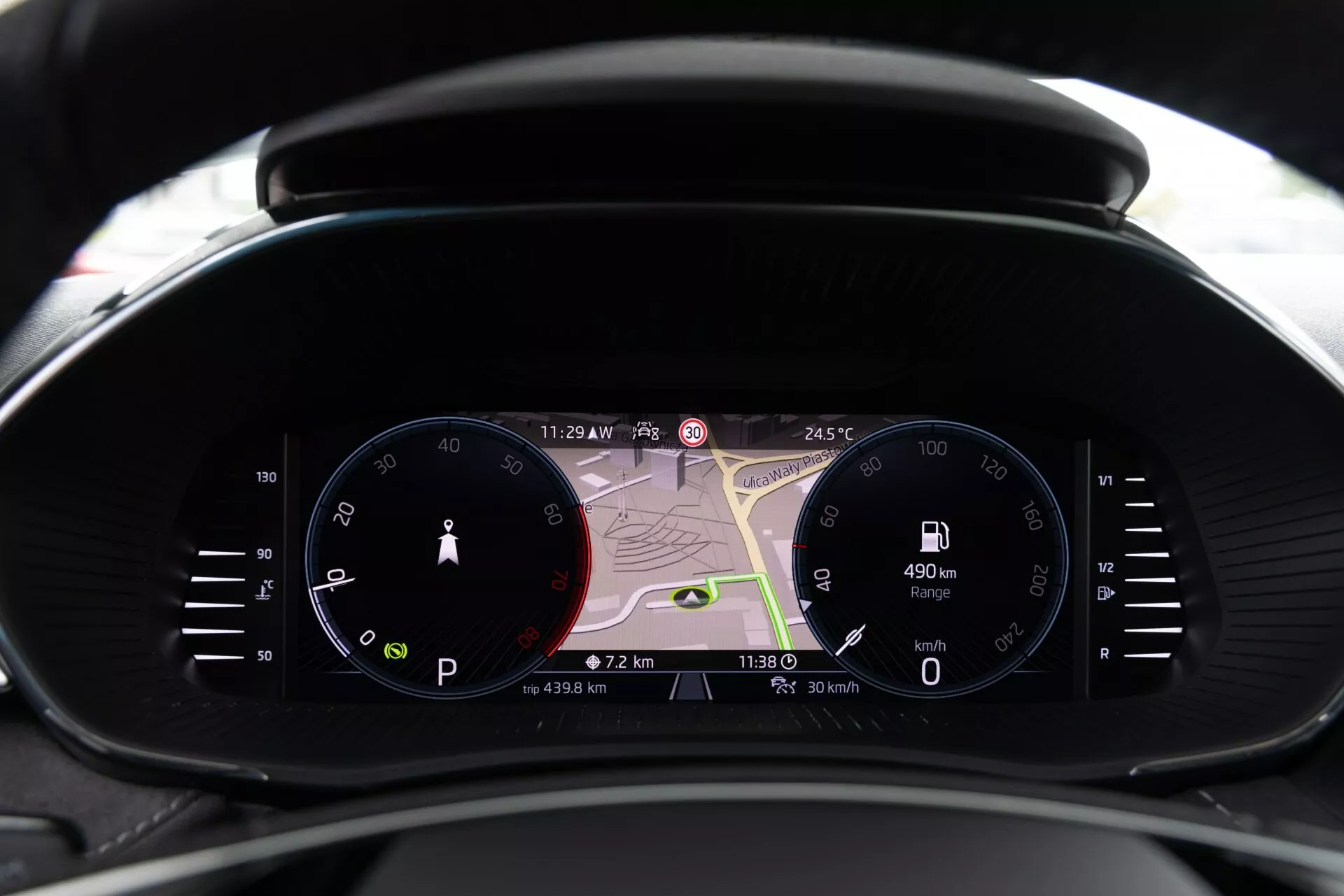 Bližnji posnetek sodobnega instrumentnega zaslona Skoda Fabia 2021 iz perspektive voznika, z analognim merilnikom hitrosti, velikim digitalnim zaslonom z navigacijsko karto in digitalnim merilnikom vrtljajev. Zasloni prikazujejo 11:29 zvečer, 24,5°C, doseg vozila 490 km, trenutno hitrost 0 km/h in podatke o potovanju. Združuje tradicionalno in sodobno oblikovanje z napredno tehnologijo, vključno z navigacijo v realnem času, informacijami za voznika in indikatorji povezljivosti.