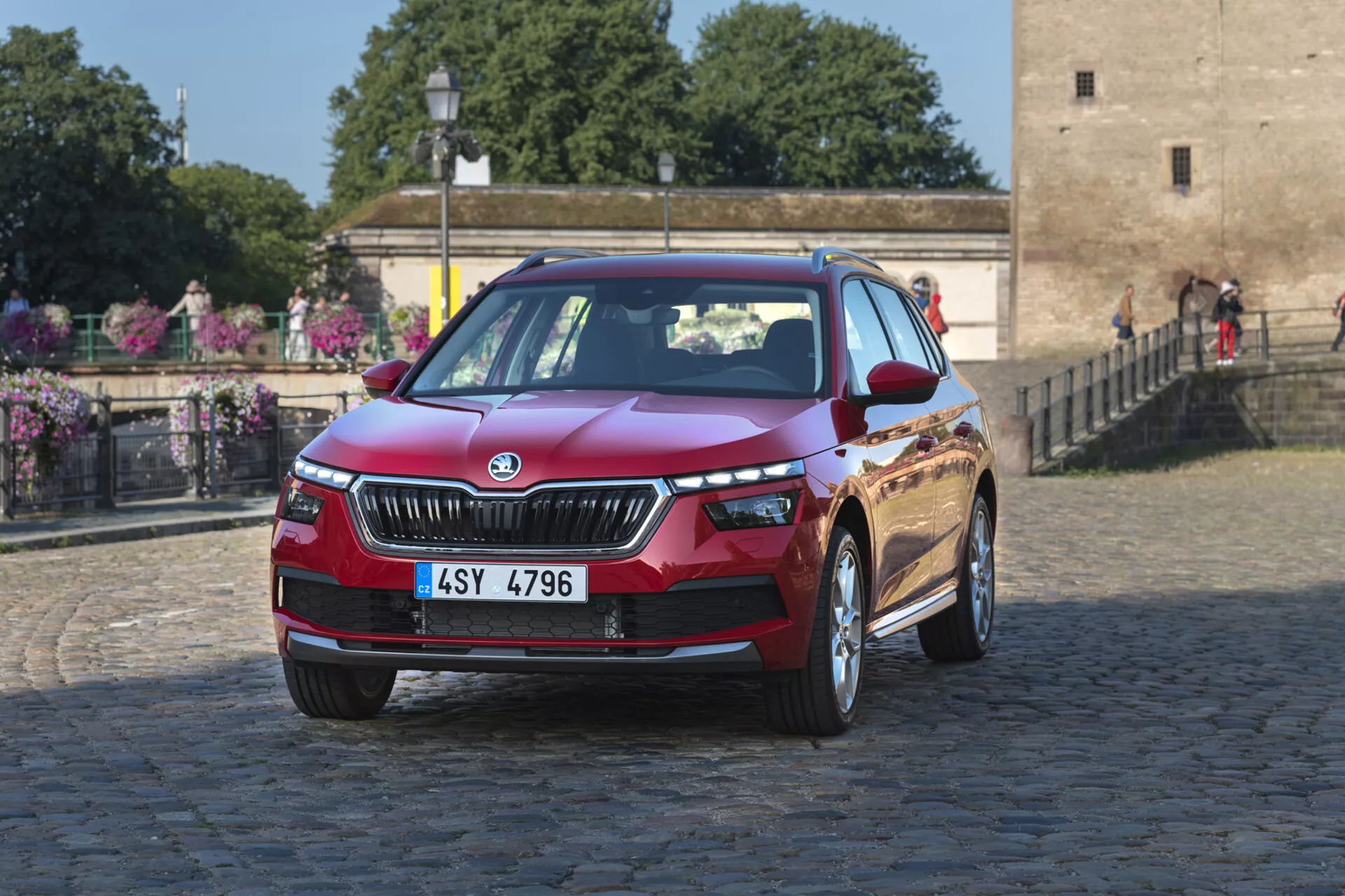 Skoda Kamiq letnik 2019 v globoko metalnično rdeči barvi, ki prikazuje oblikovalske značilnosti kot so rešetka, LED žarometi in lita platišča na mestnem ozadju tlakovcev