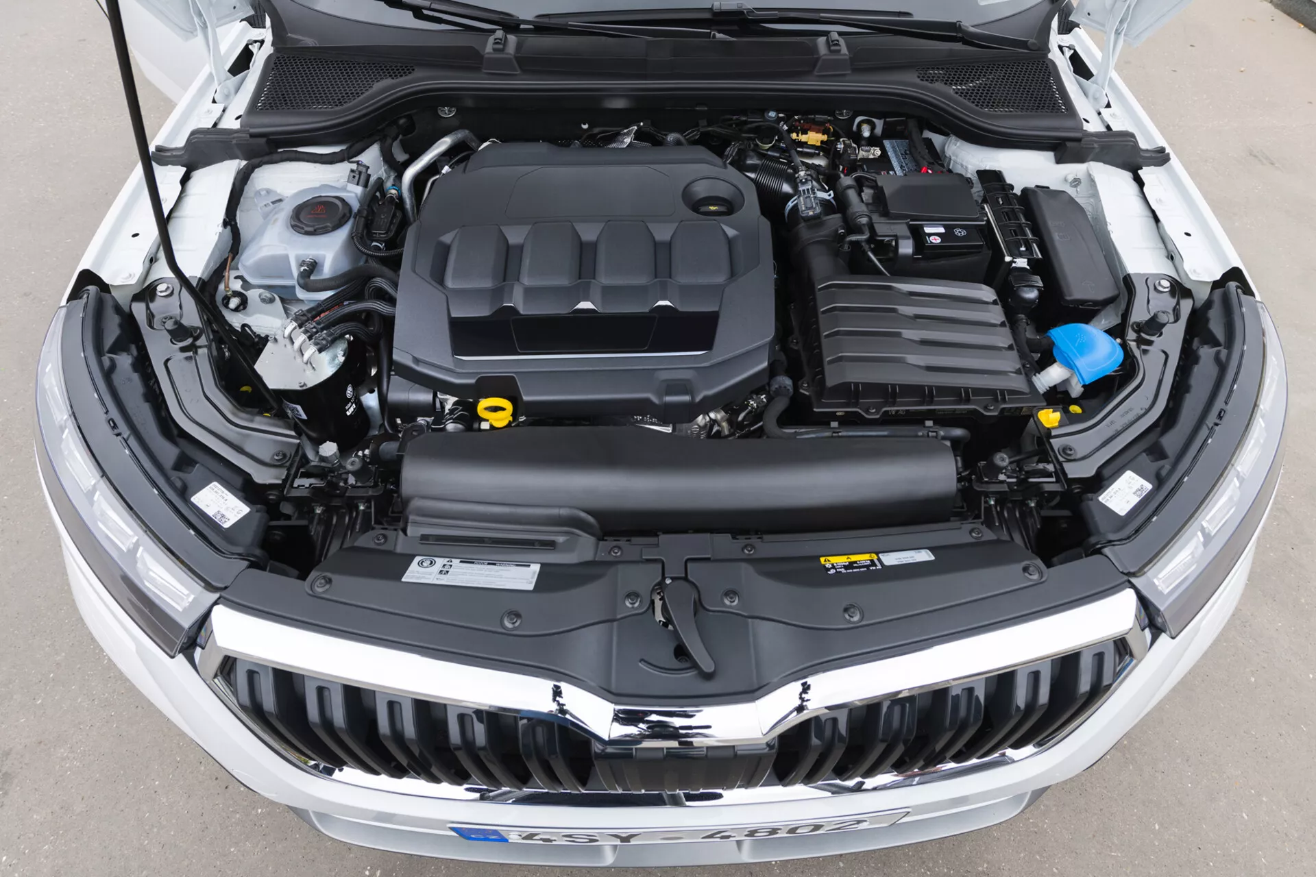 Ptičja perspektiva motorja Skoda Kamiq 2019 z odprtim pokrovom, ki prikazuje pokrov motorja, sistem za dovod zraka, baterijo, rezervoar za hladilno tekočino in različne druge komponente jasno vidne, idealno za izobraževanje o avtomobilski tehnologiji in vzdrževanju vozil