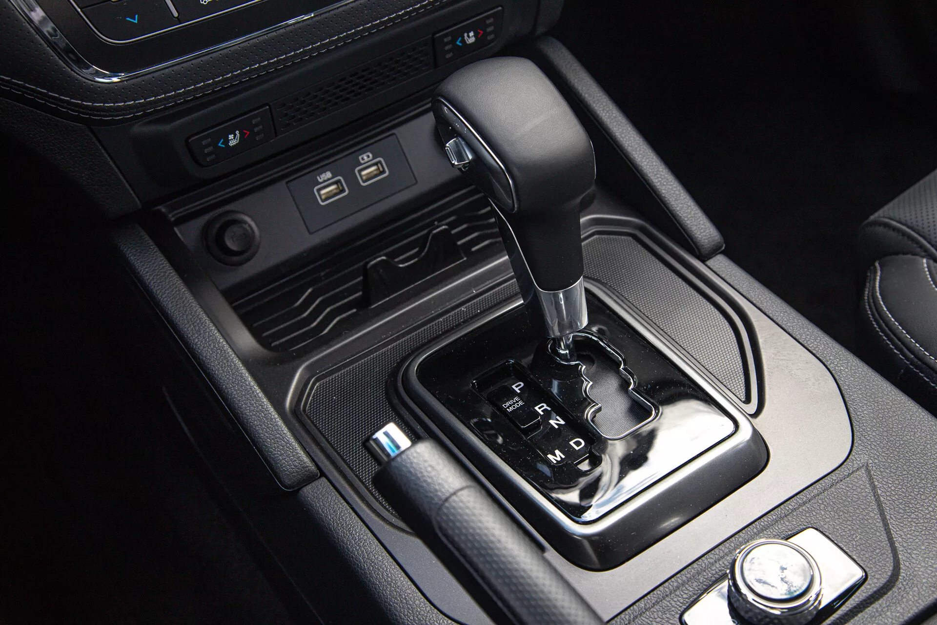 Notranjost SsangYong Musso Grand Pickup 2022 s sredinsko konzolo, ki prikazuje avtomatski izbirnik prestav, moderne povezovalne vhode in kontrolnike načinov vožnje, obdano z usnjenimi in kovinskimi poudarki